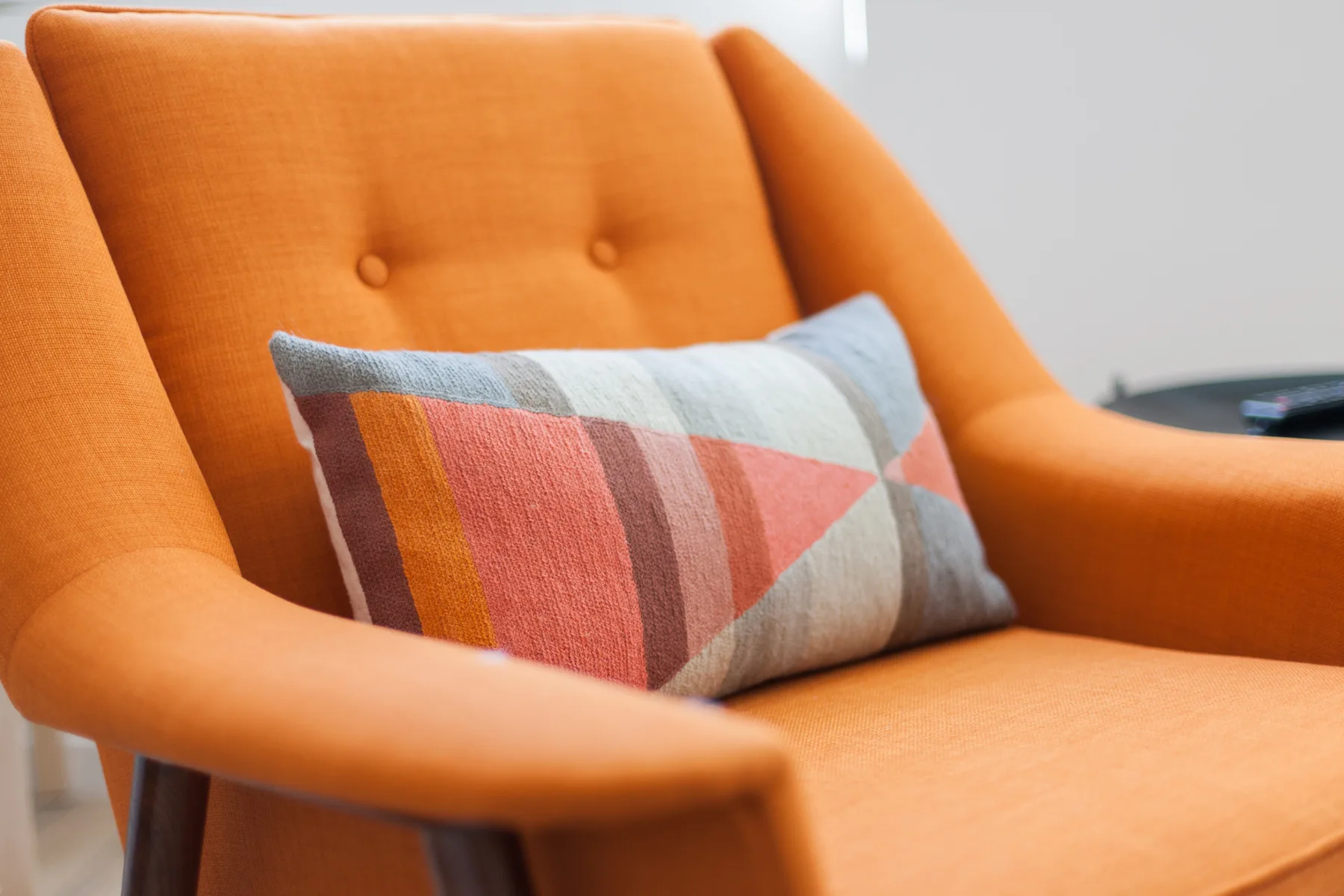 A bright orange armchair with a patterned cushion.