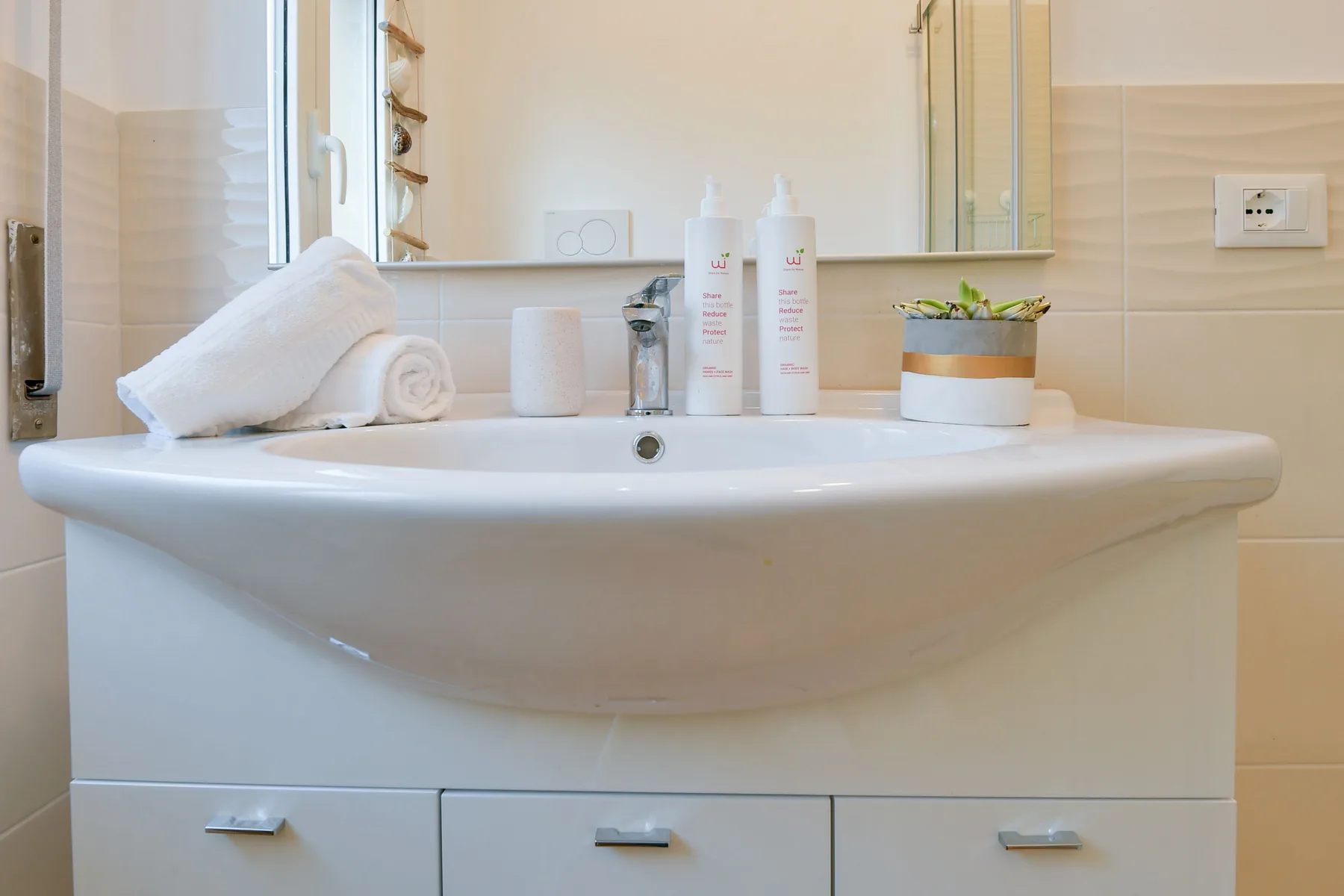 Un tocador de baño con lavabo, artículos de aseo y una pequeña planta en maceta.