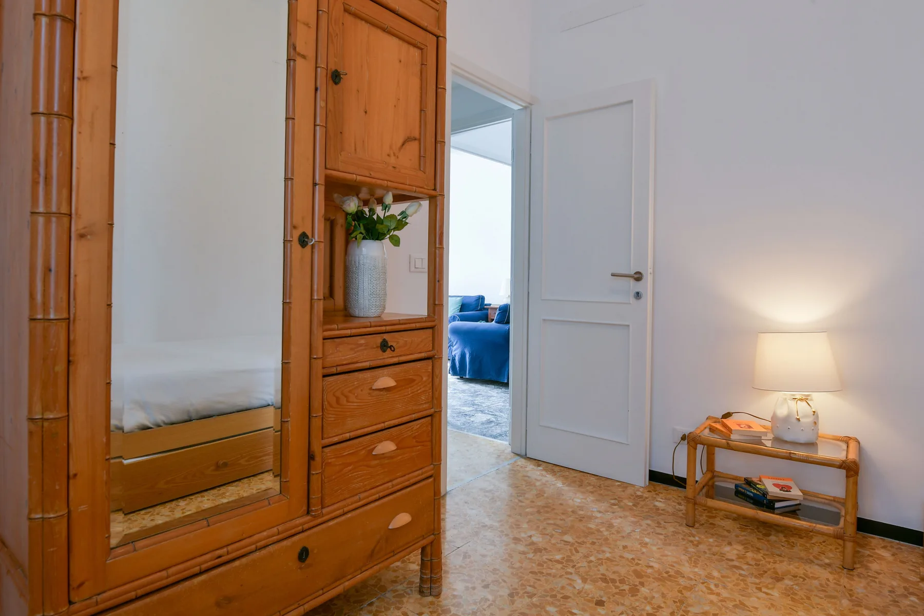 Una puerta abierta da a un dormitorio, junto a muebles de madera y una lámpara encendida.