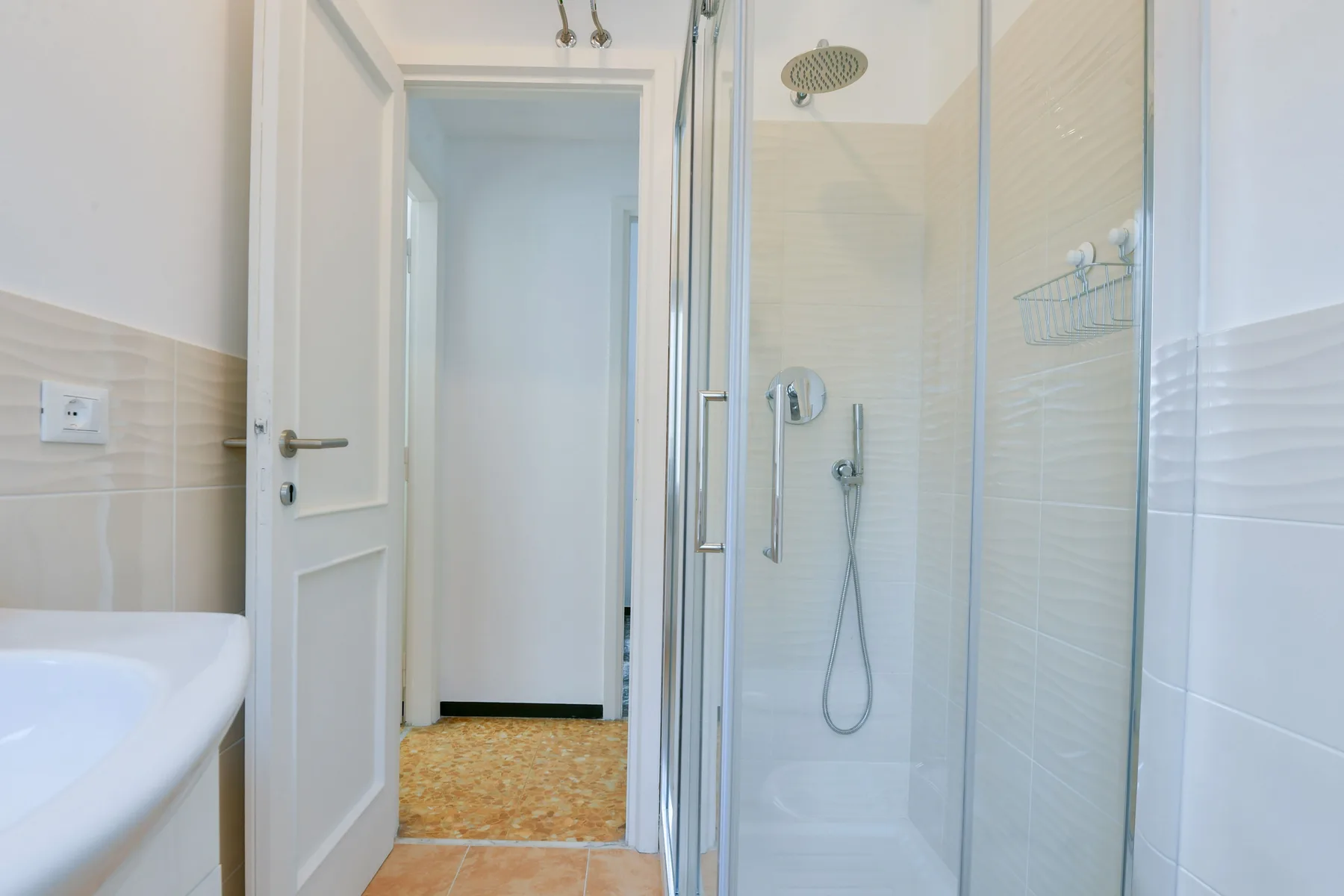 Un baño alicatado con una ducha de vidrio y una puerta abierta al pasillo.