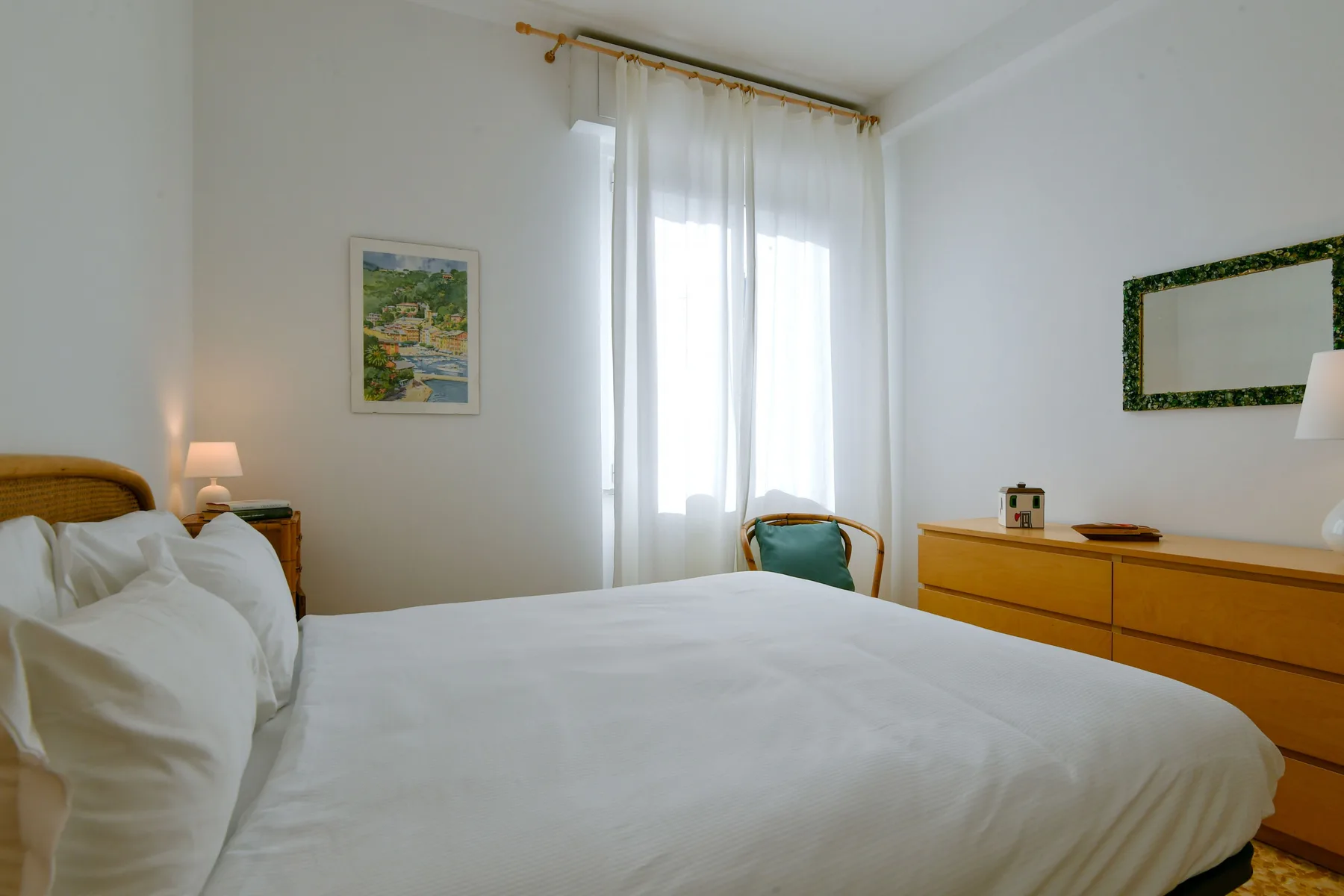 Un dormitorio luminoso con una cama bien hecha y cortinas translúcidas.