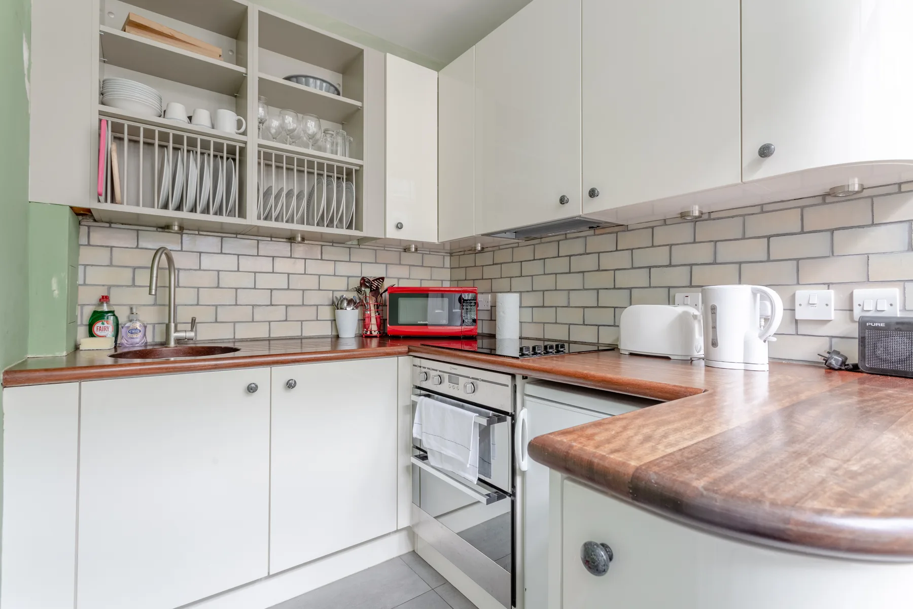 Una cocina luminosa con armarios blancos, estantes abiertos para platos y encimeras de madera.