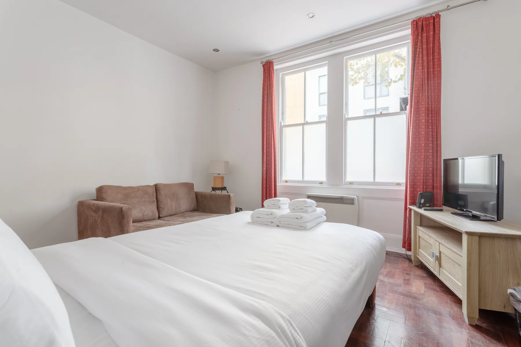 Un dormitorio luminoso con una cama bien hecha, asientos y un televisor.