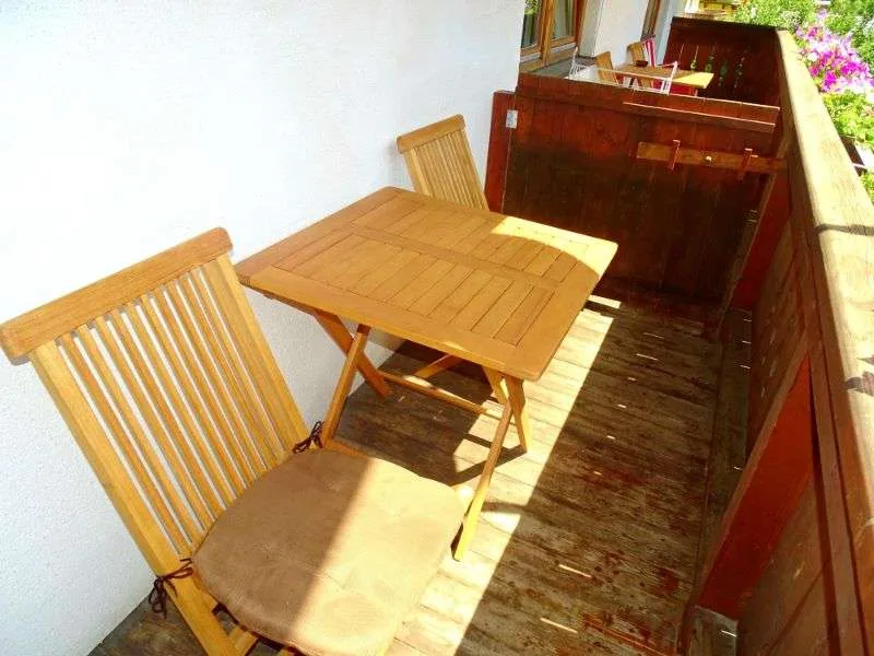 A narrow outdoor balcony has a wooden table and seating.