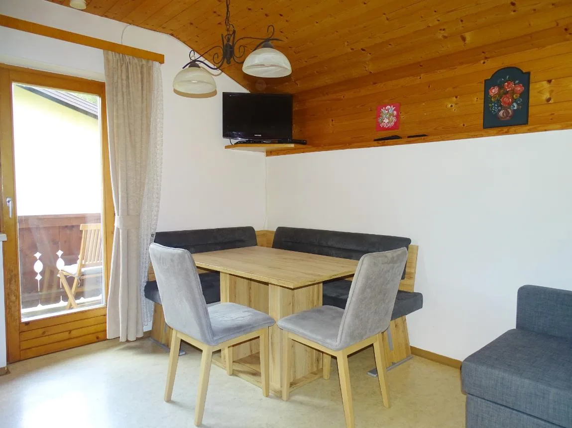 Un comedor con una mesa de madera, asientos tapizados y una puerta al balcón.