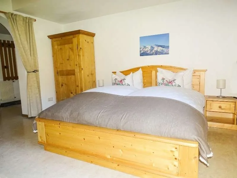 A bedroom with a large bed, wooden furnishings, and a mountain picture on the wall.