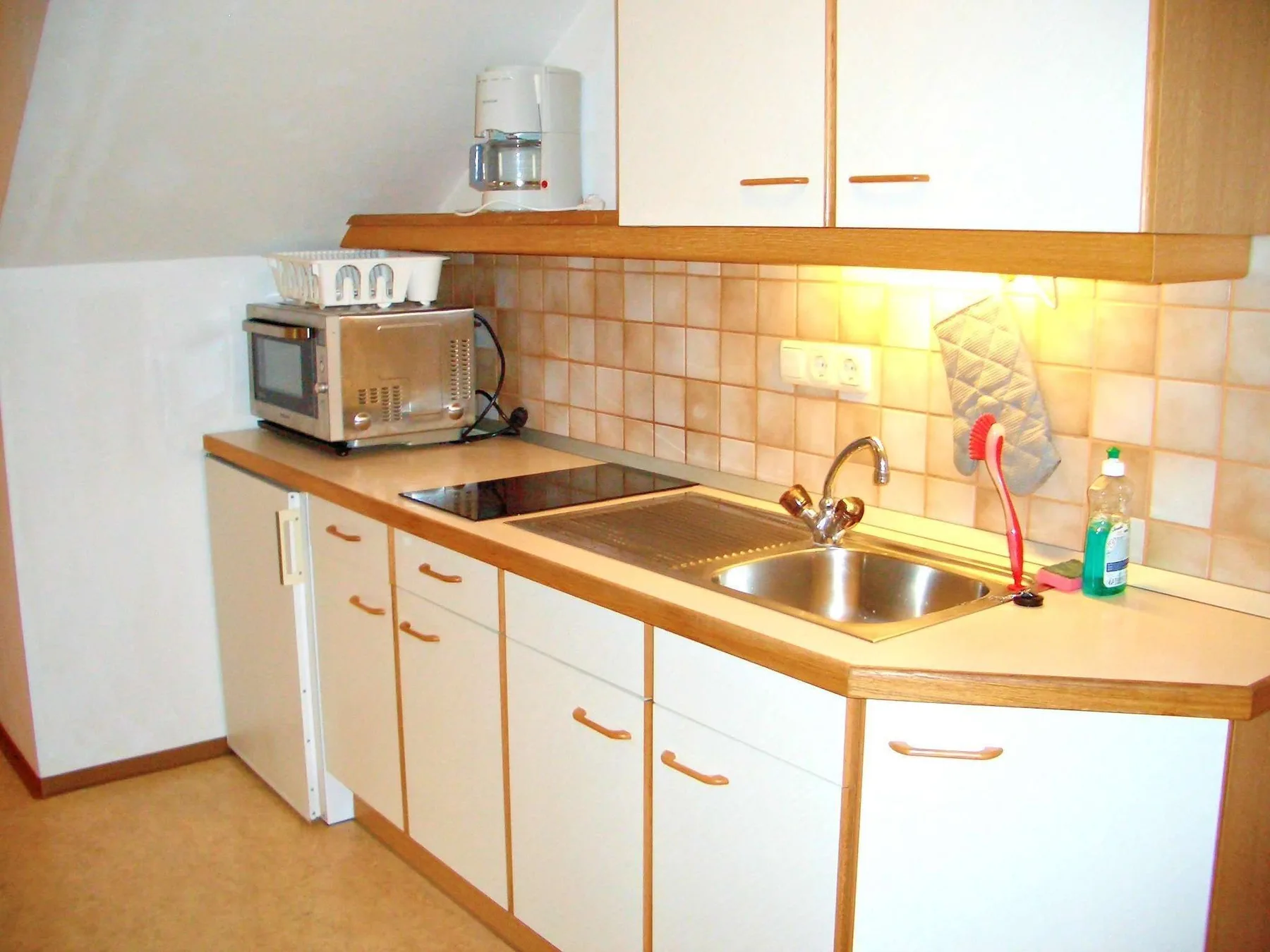 Una cocina compacta con encimera, fregadero y armarios superiores.