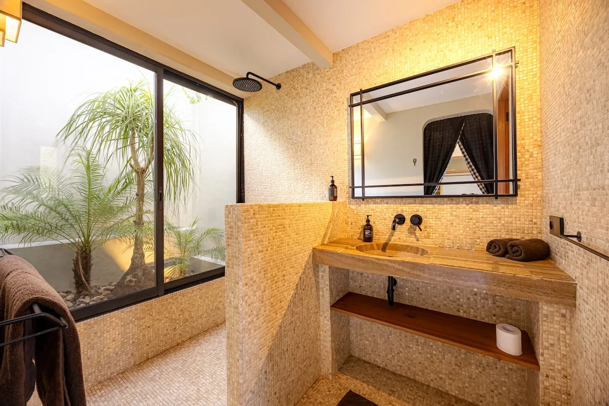 A tiled bathroom vanity with a large mirror beside a glass window.