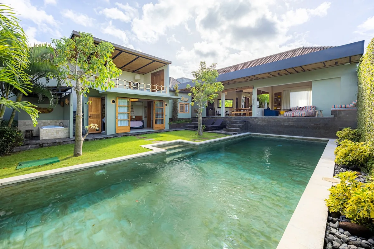 A modern house opens onto a rectangular swimming pool and a green lawn.