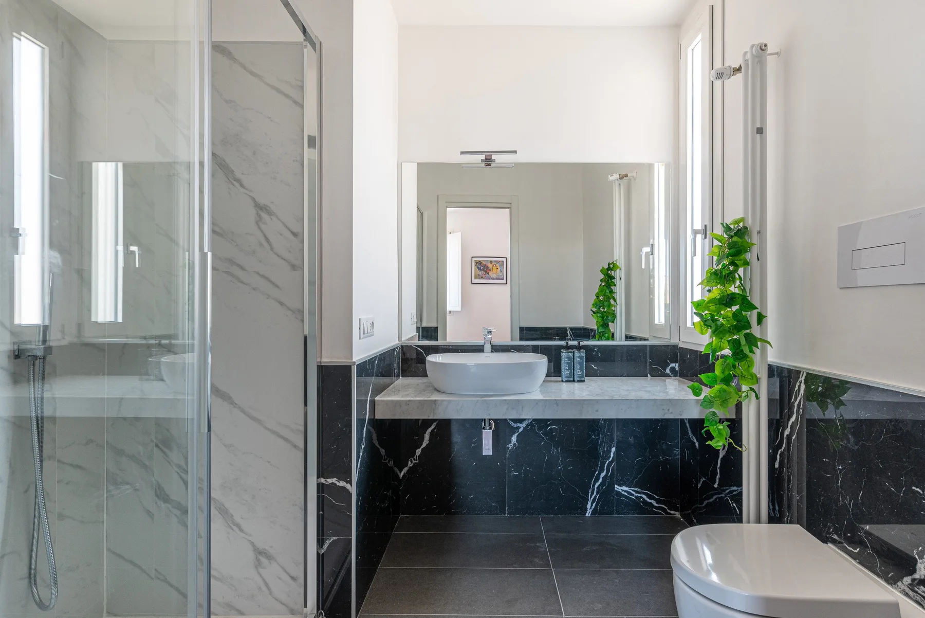 Un baño moderno con una ducha de vidrio y un amplio espejo sobre el lavabo.