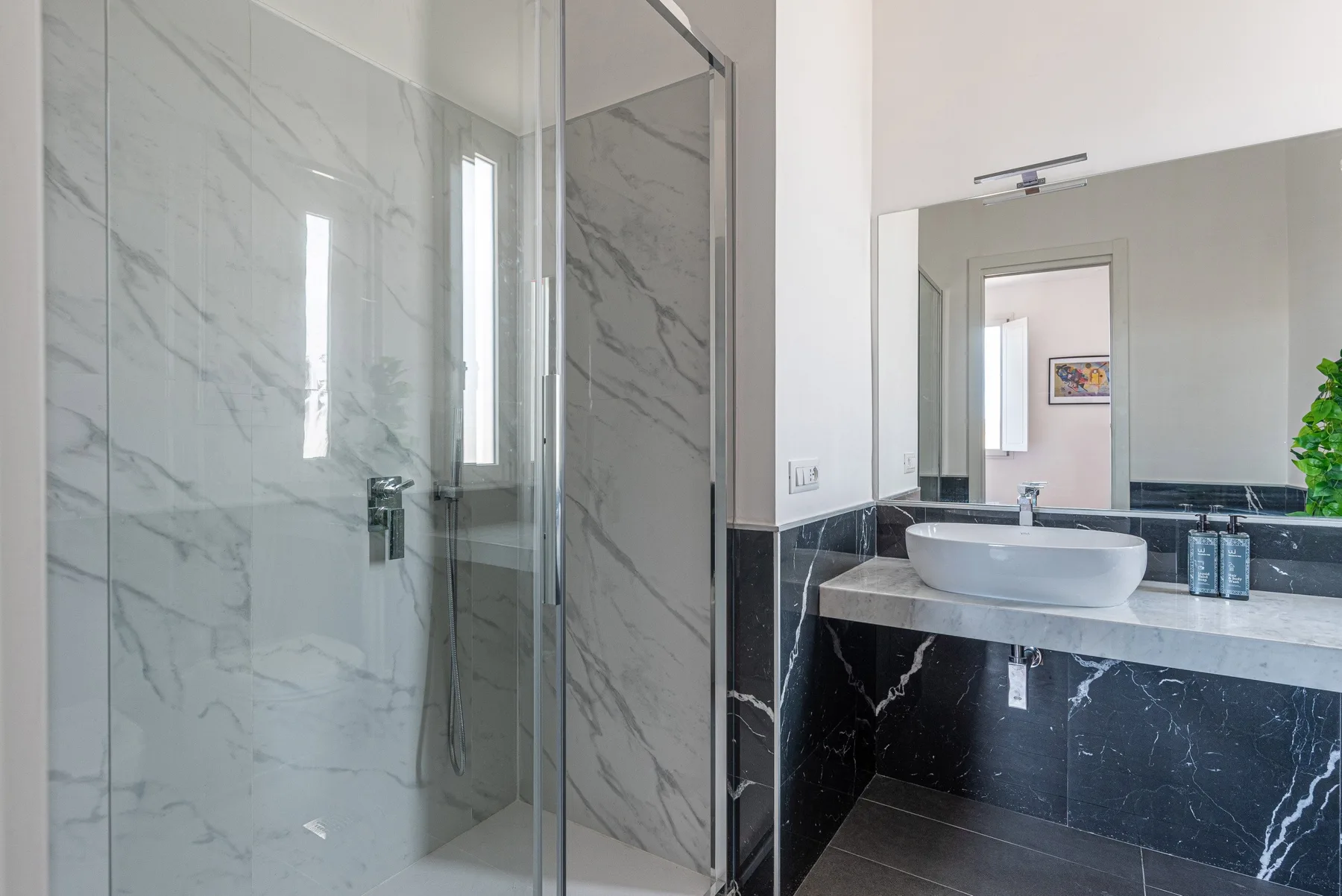 Un baño moderno con ducha de vidrio y lavabo bajo un espejo grande.