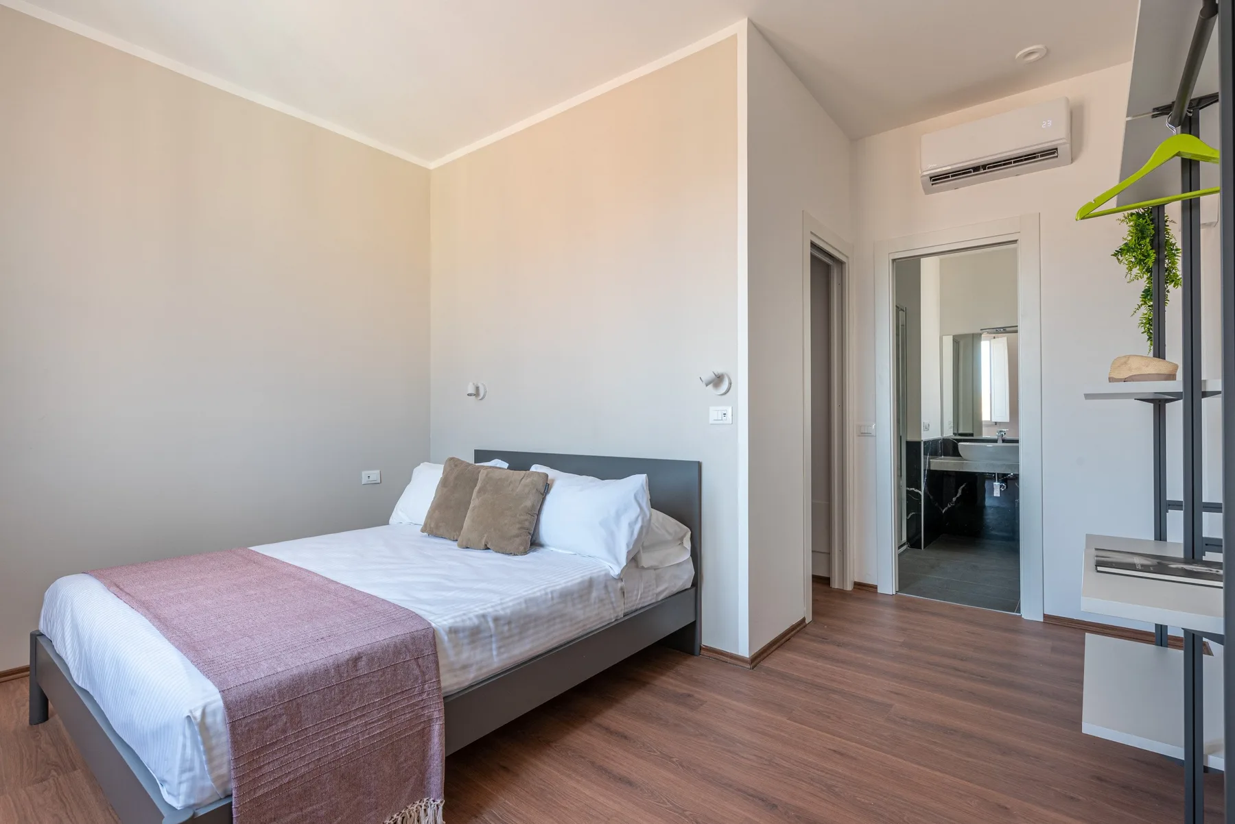 Un dormitorio con una cama, paredes claras y una puerta que da a un baño.