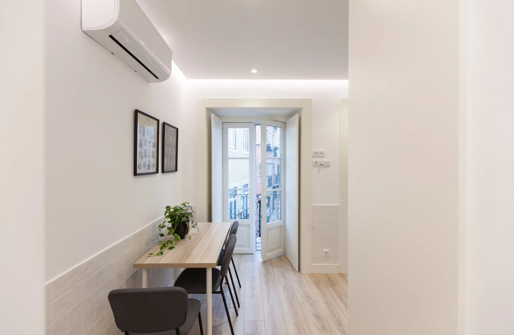A narrow dining area with a wooden table and chairs leads to a glass balcony door.