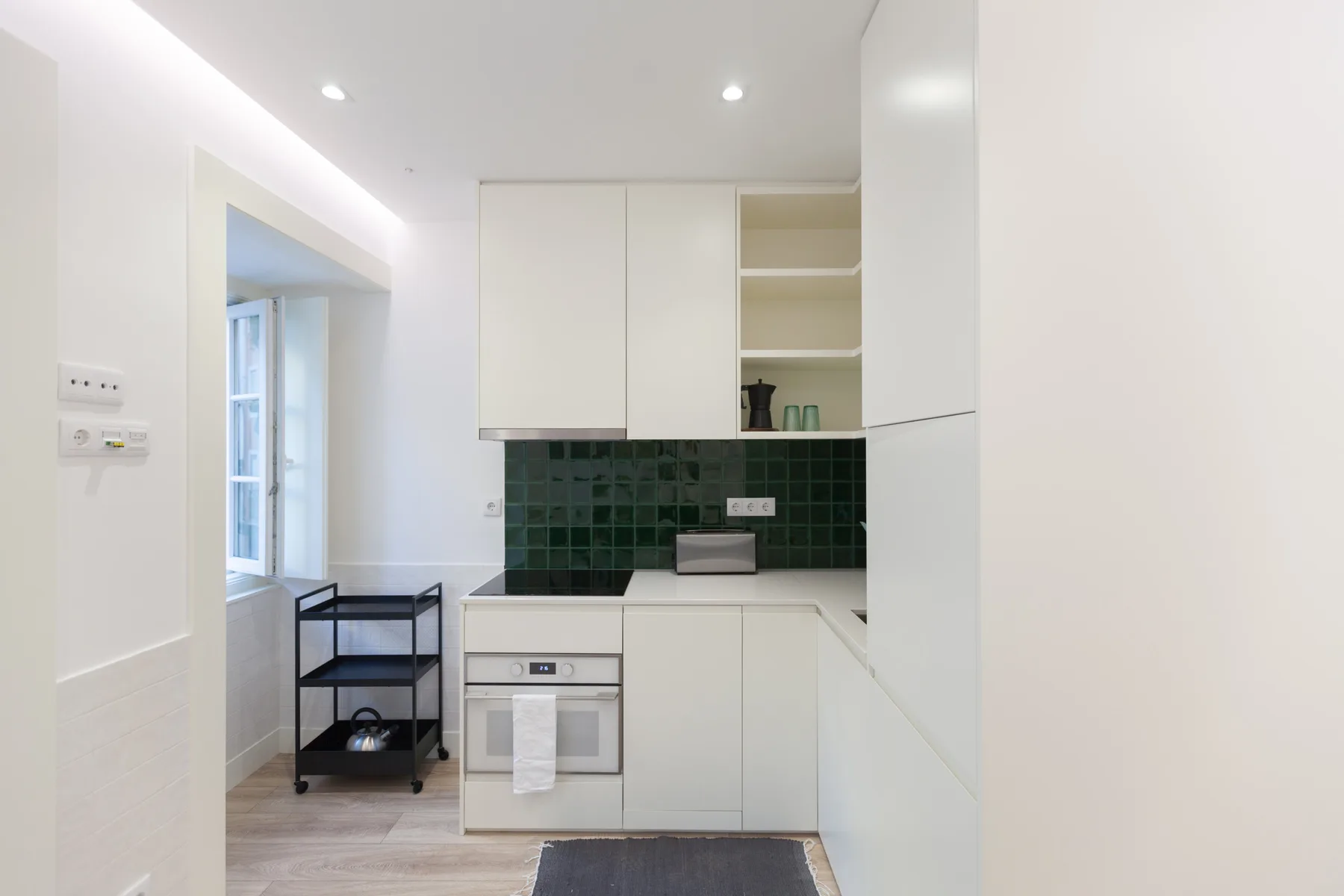 A compact kitchen with white cabinets, dark green tile, and a countertop.