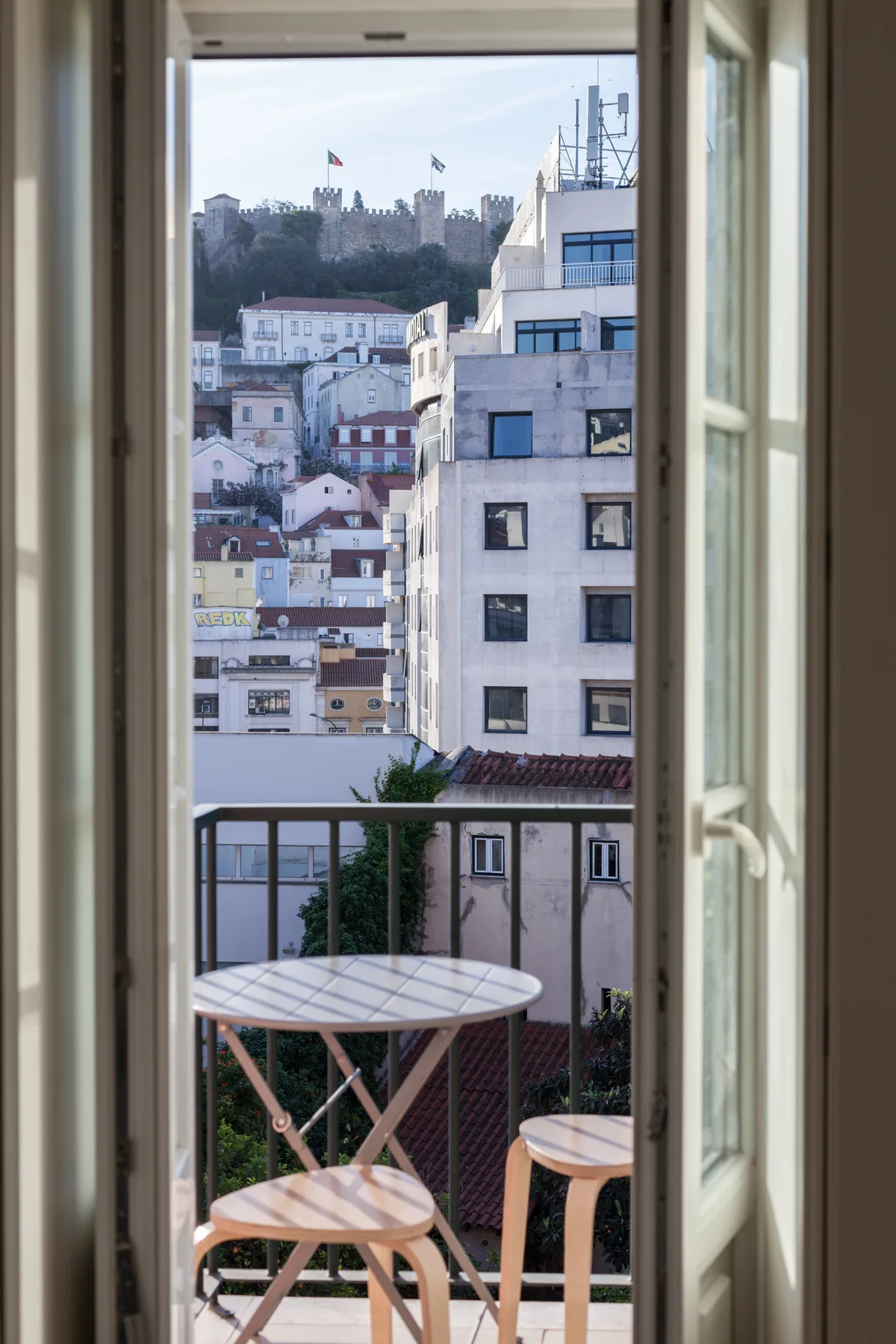 A city view from a balcony, with a round table and nearby buildings.