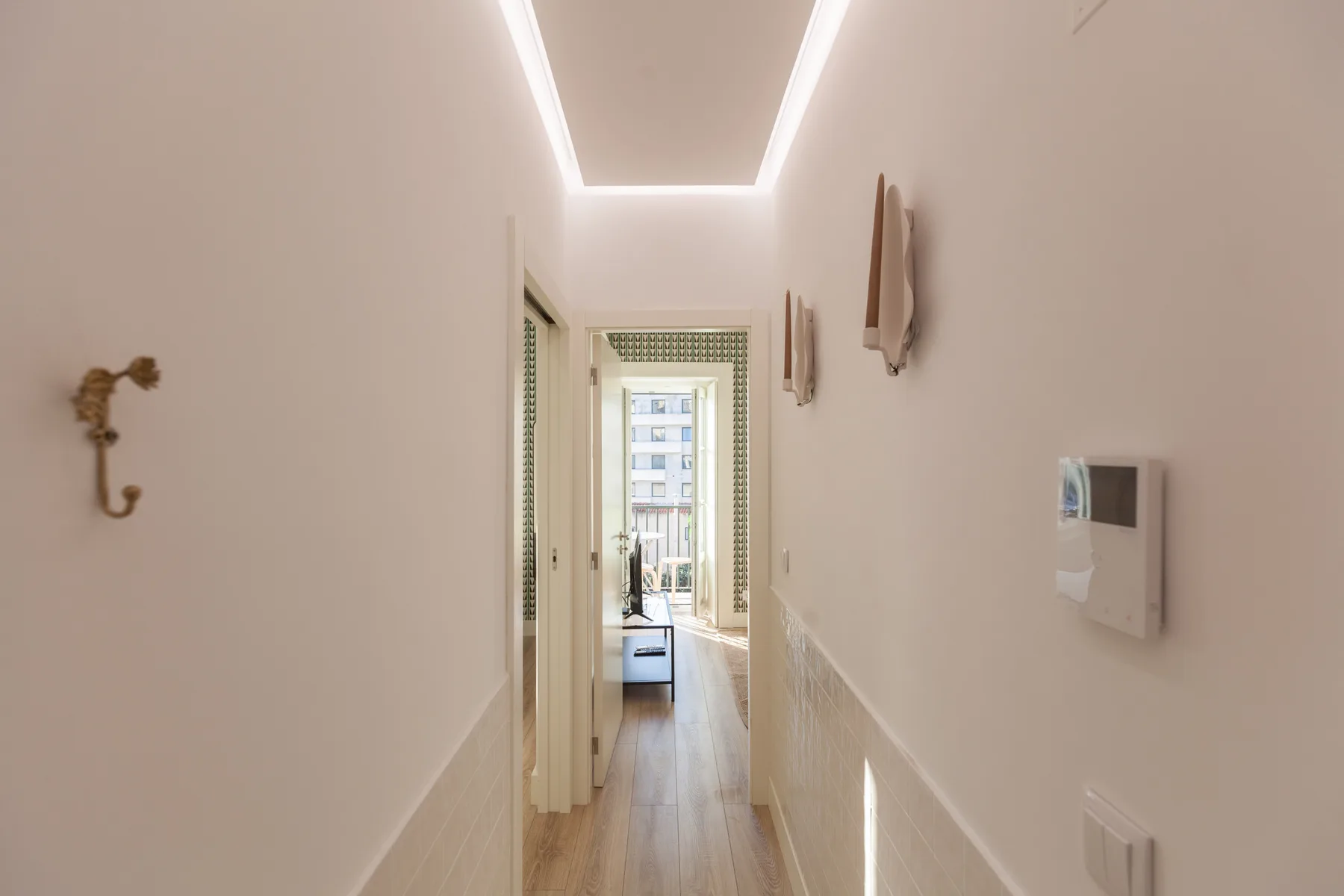 A narrow hallway with wood flooring leads to a bright room at the end.