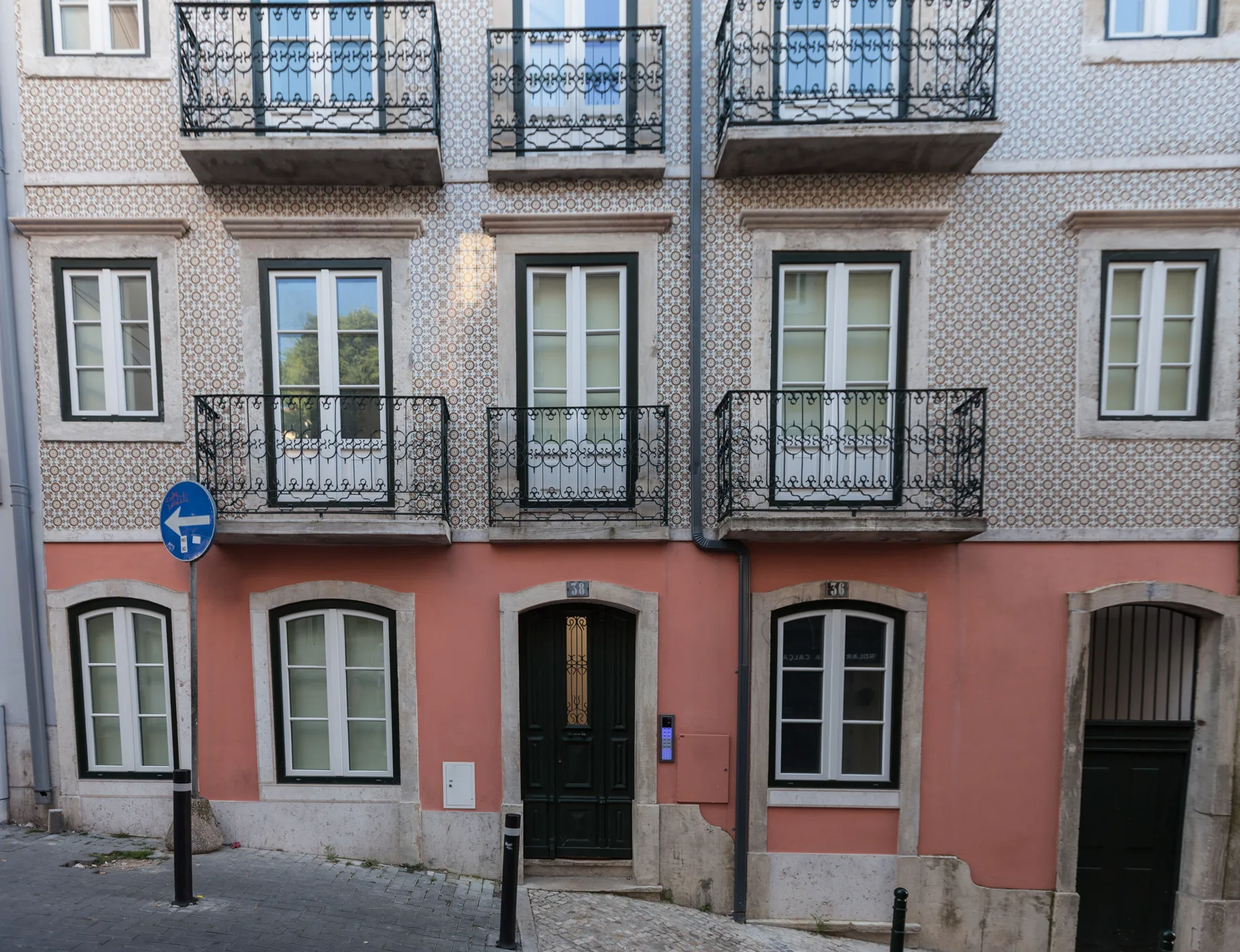A tiled urban building facade has balconies, windows, and street-level entrances.
