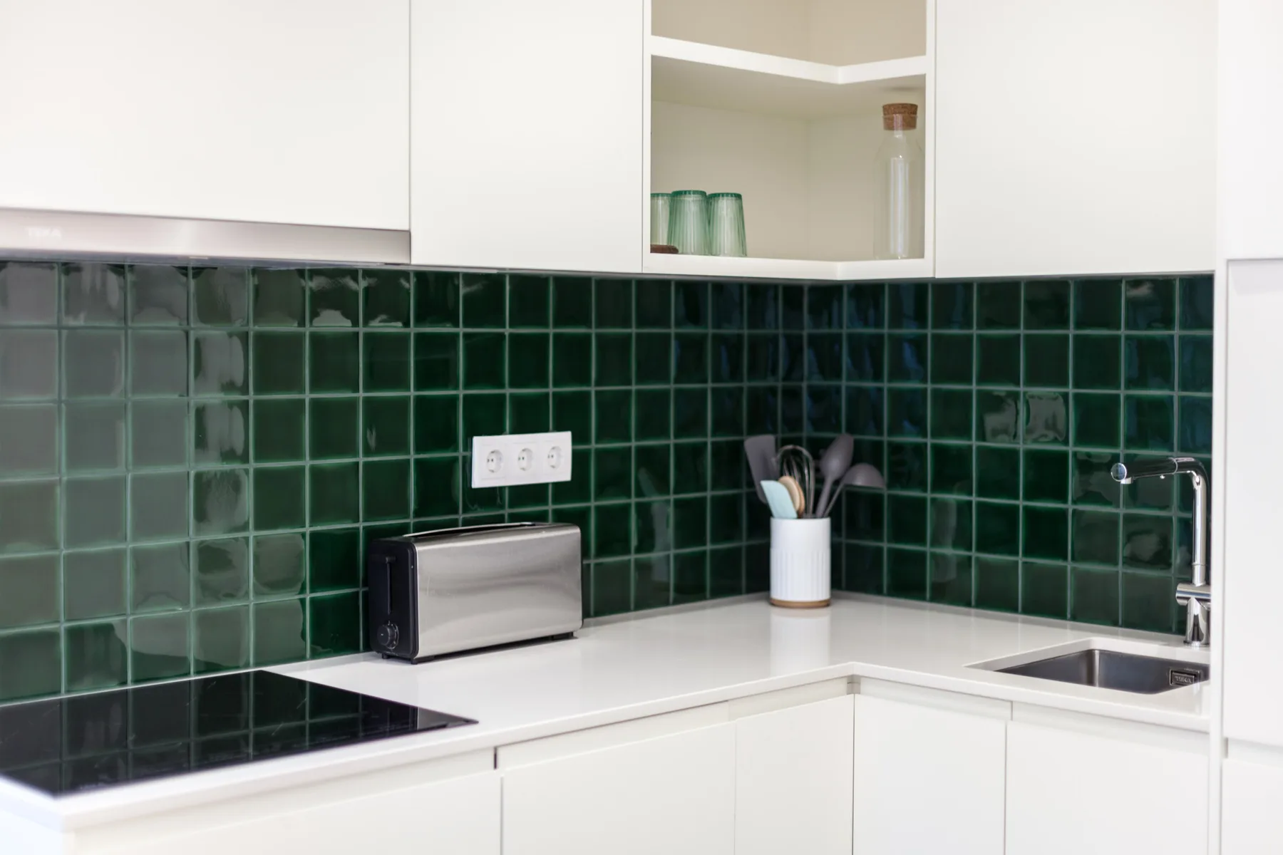A bright kitchen with white cabinets and dark green tile backsplash.