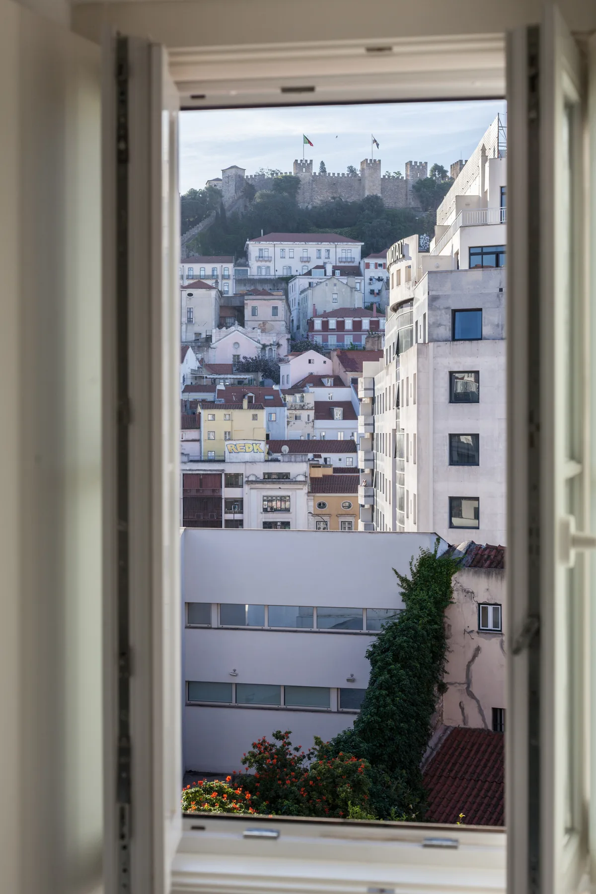 An open window frames nearby buildings and a hilltop castle.