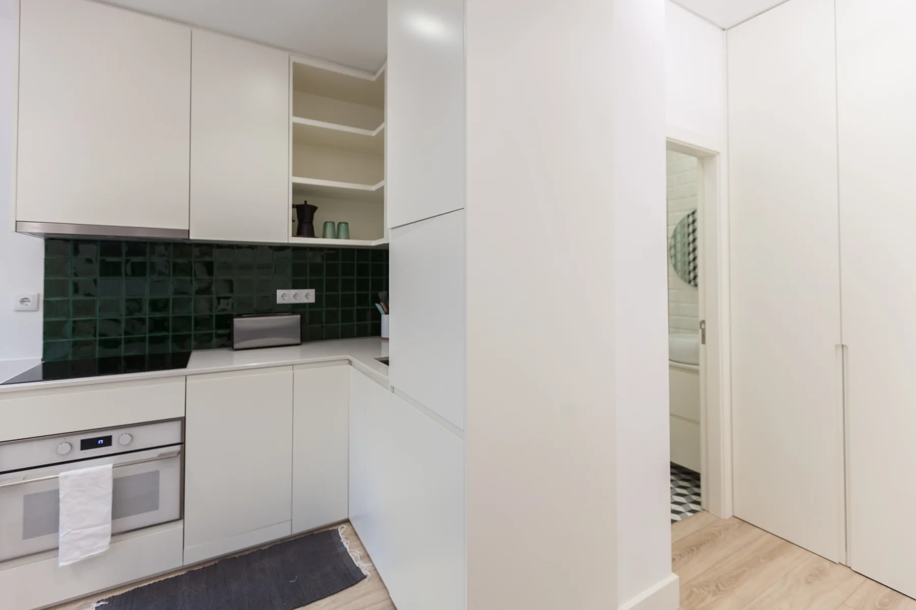 A bright kitchen with white cabinets, dark backsplash, and an oven.