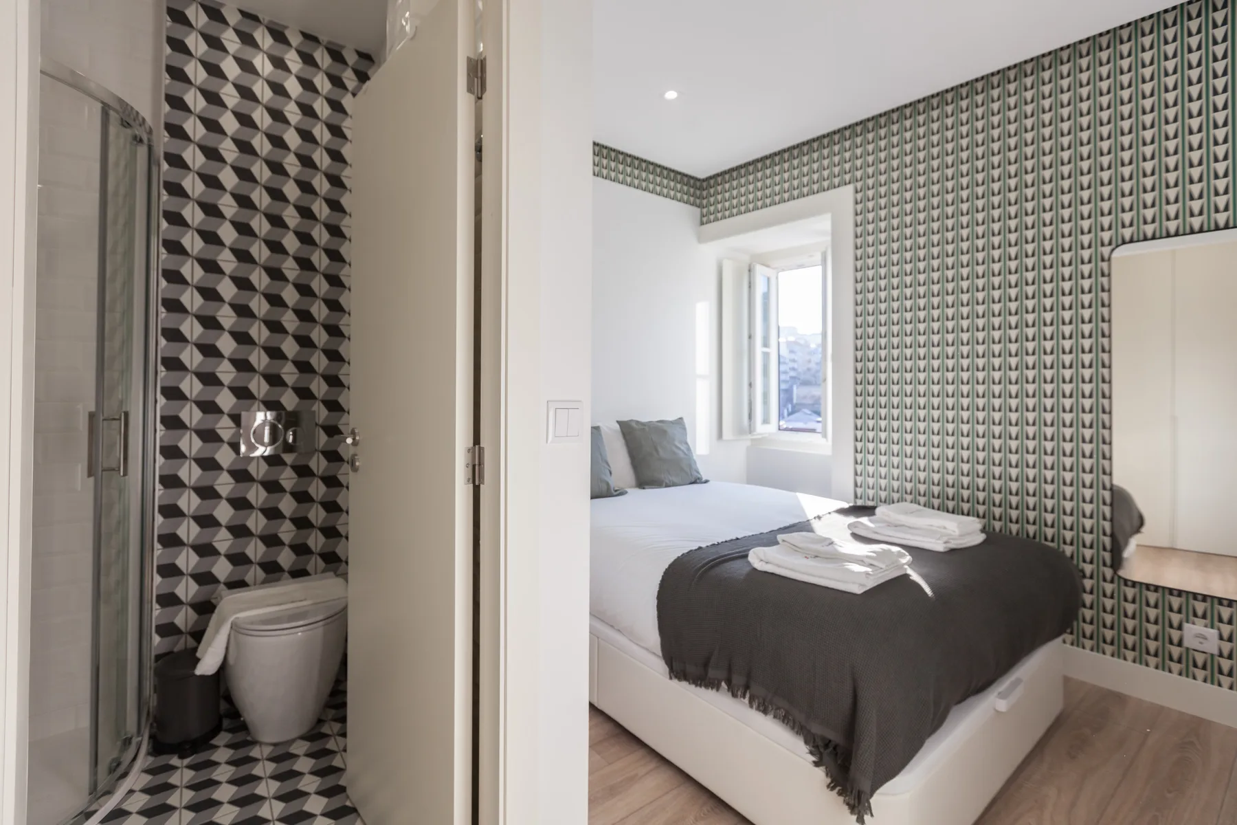 A bedroom with patterned wallpaper, a bed, and an adjoining bathroom.