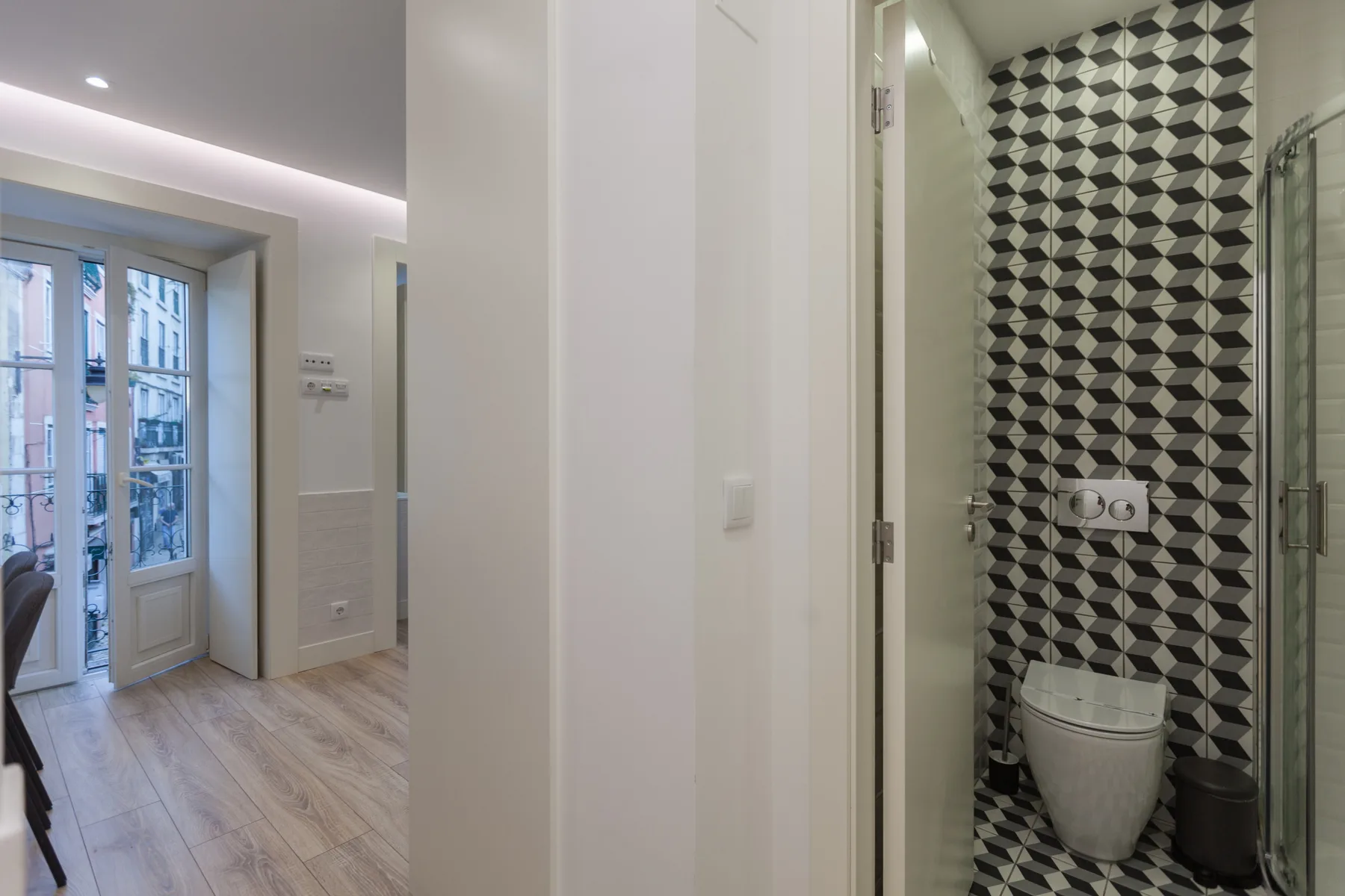 A bright apartment interior with a glass-door shower and a windowed sitting area.