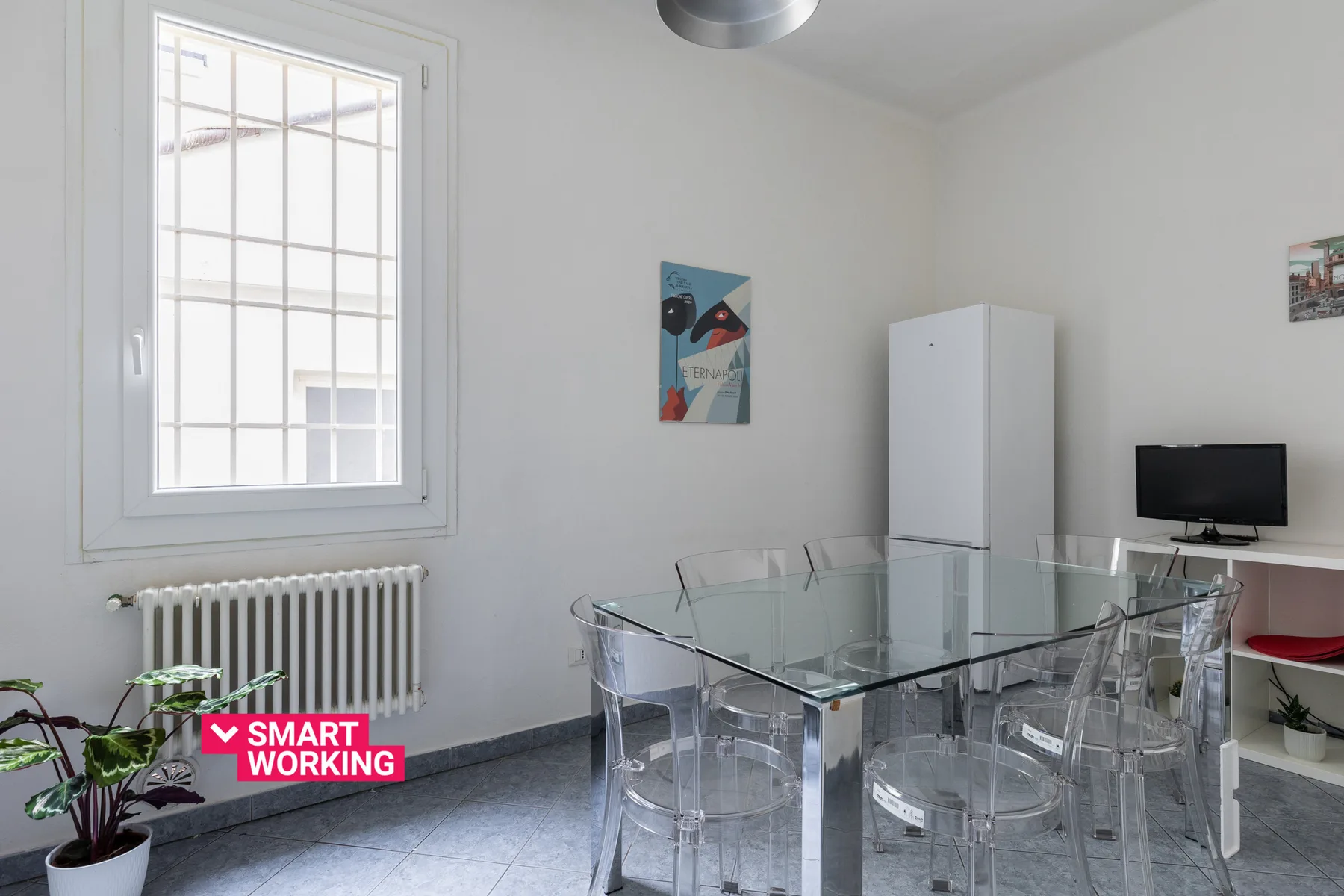 A bright dining area with a glass table, clear seating, and a tall window.