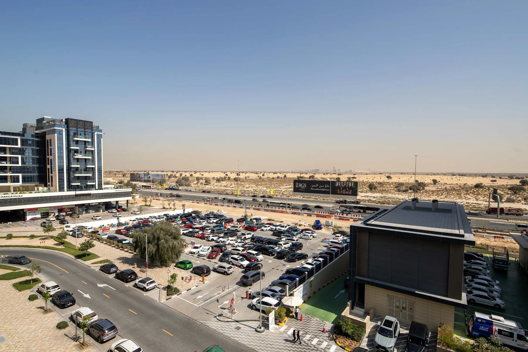 Urban commercial scene with a large parking lot, office buildings, and desert landscape beyond.