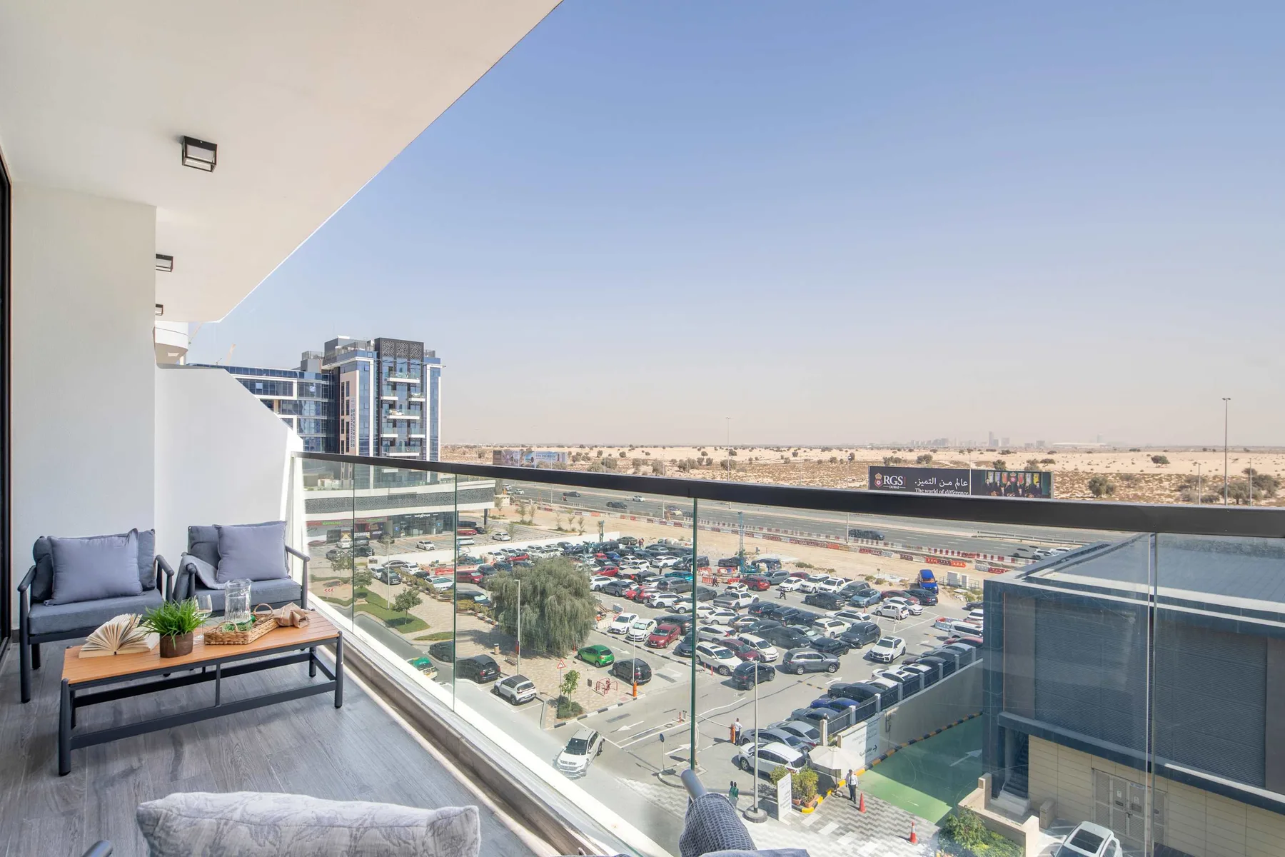 A balcony seating area overlooks a large parking lot and distant buildings.
