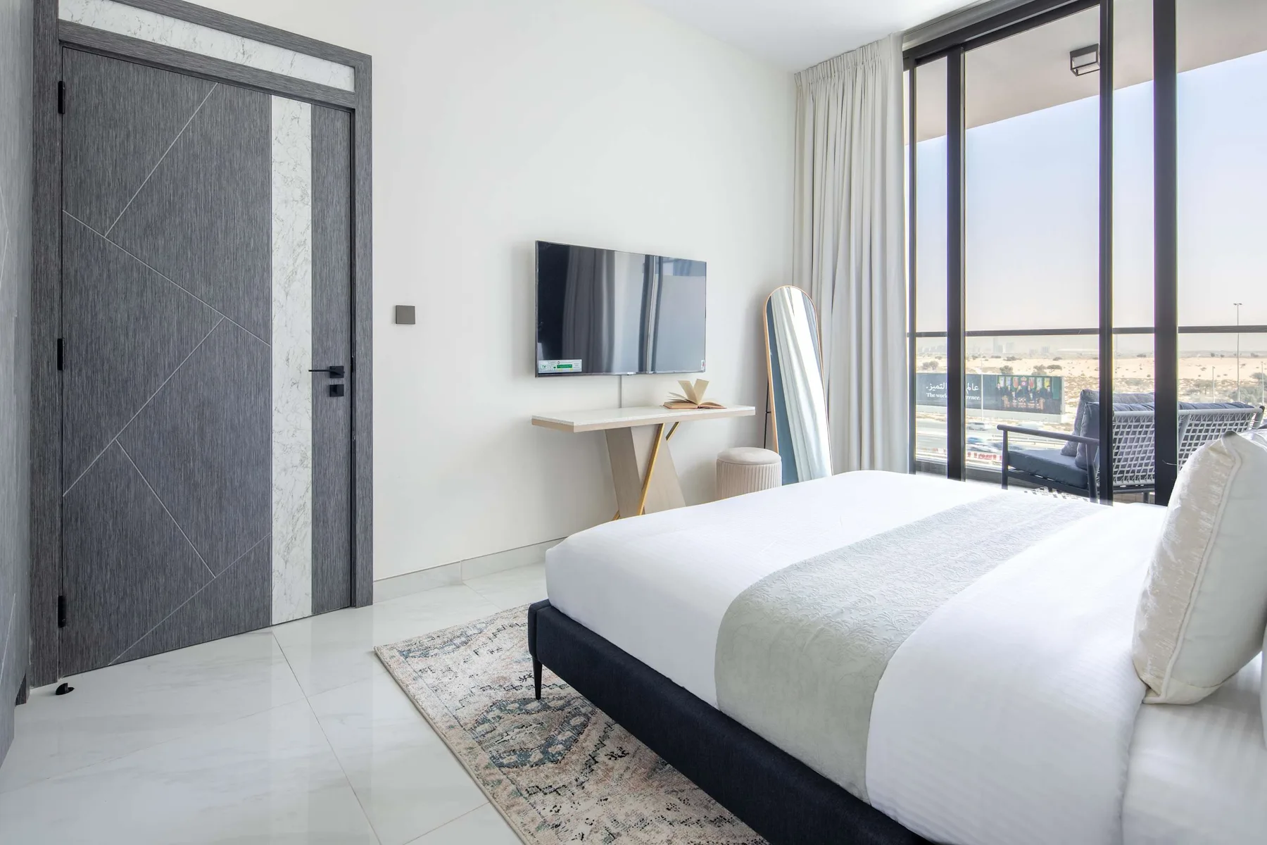 A bright bedroom with a bed, wall-mounted television, and sliding glass doors.