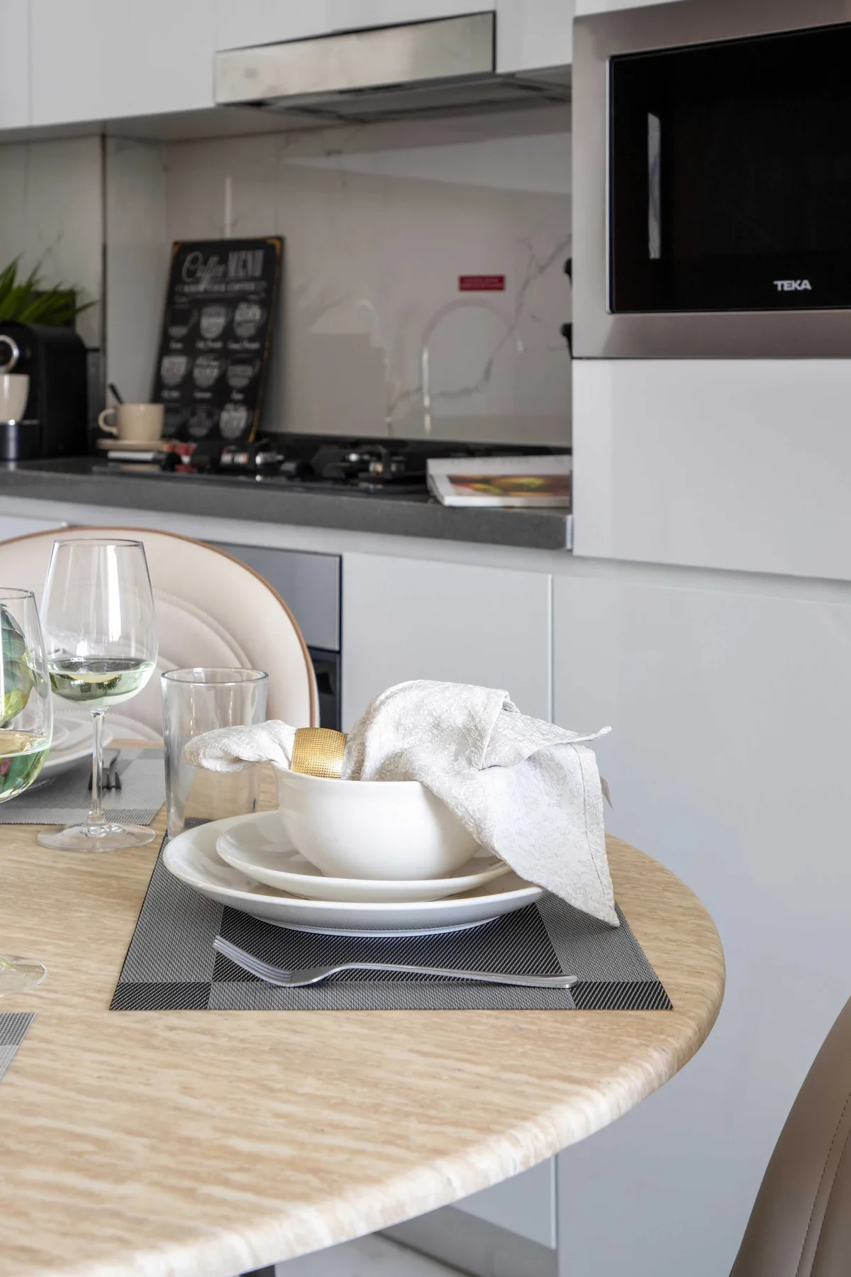 A dining table with place settings sits in front of a modern kitchen.