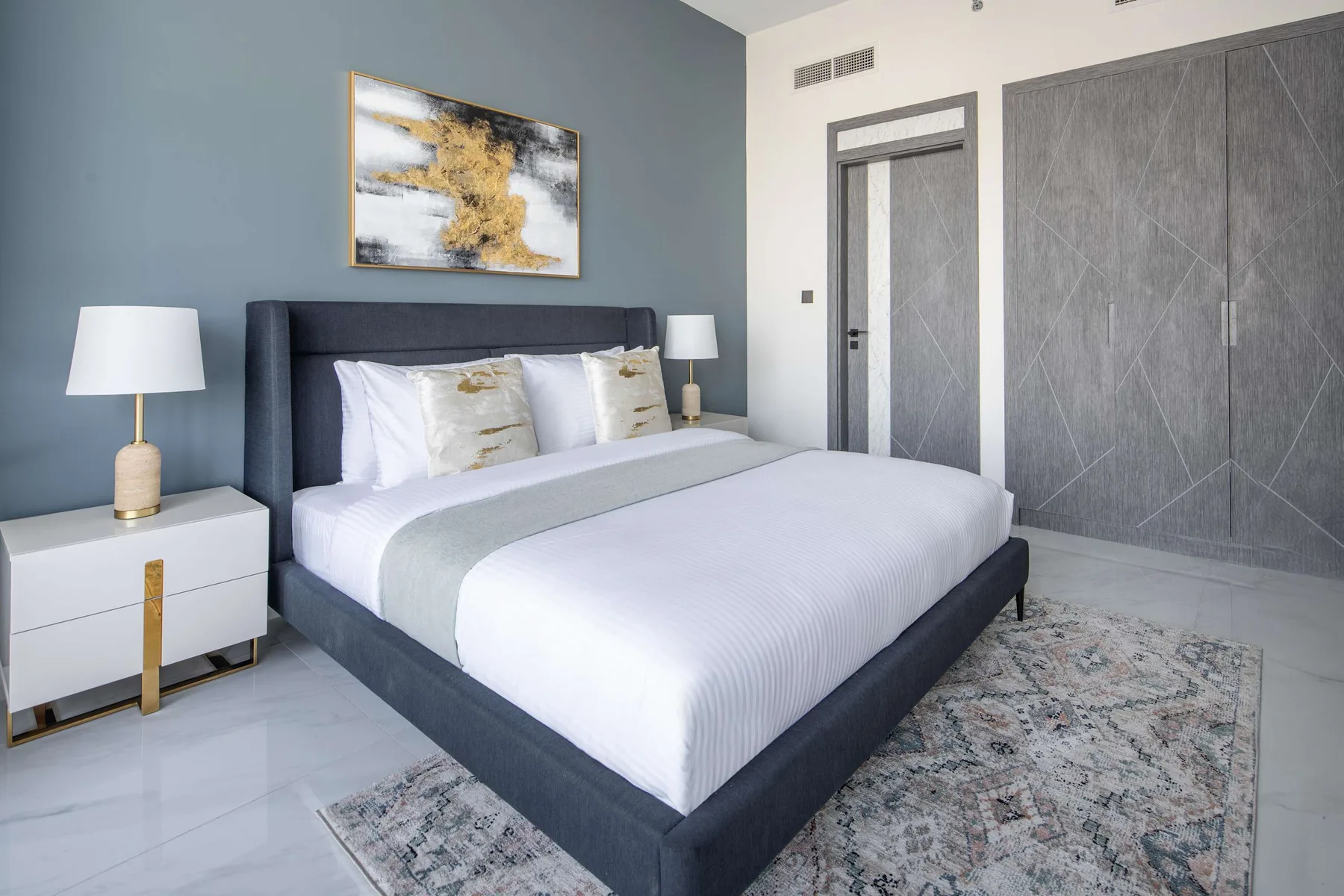 A bedroom with a neatly made bed, bedside tables, and abstract wall art.