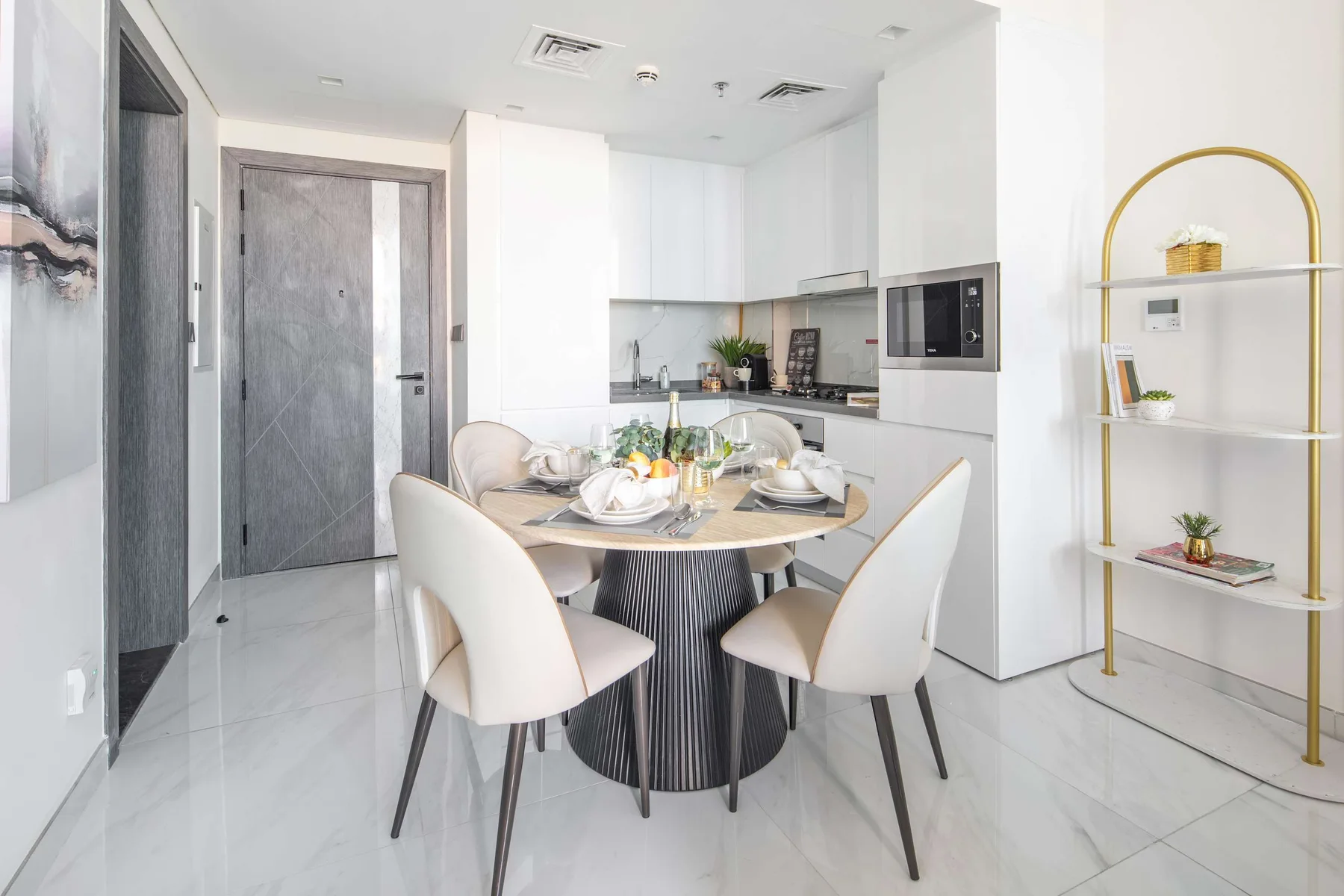 A bright dining area with a set table and a compact kitchen in the background.