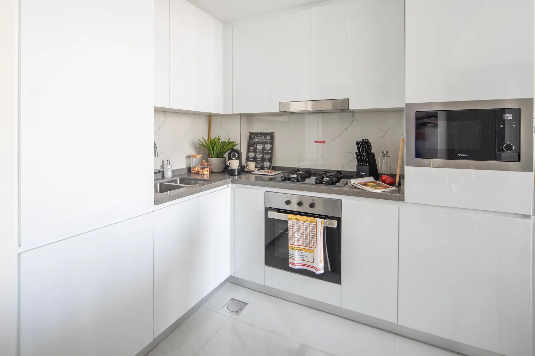 A modern kitchen with white cabinets, a cooktop, and built-in appliances.
