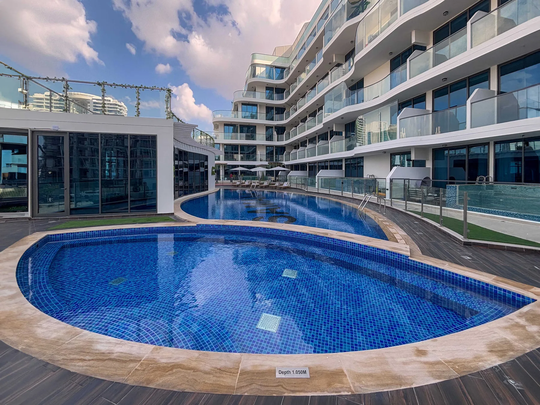 A curved swimming pool sits beside a modern multi-story building.