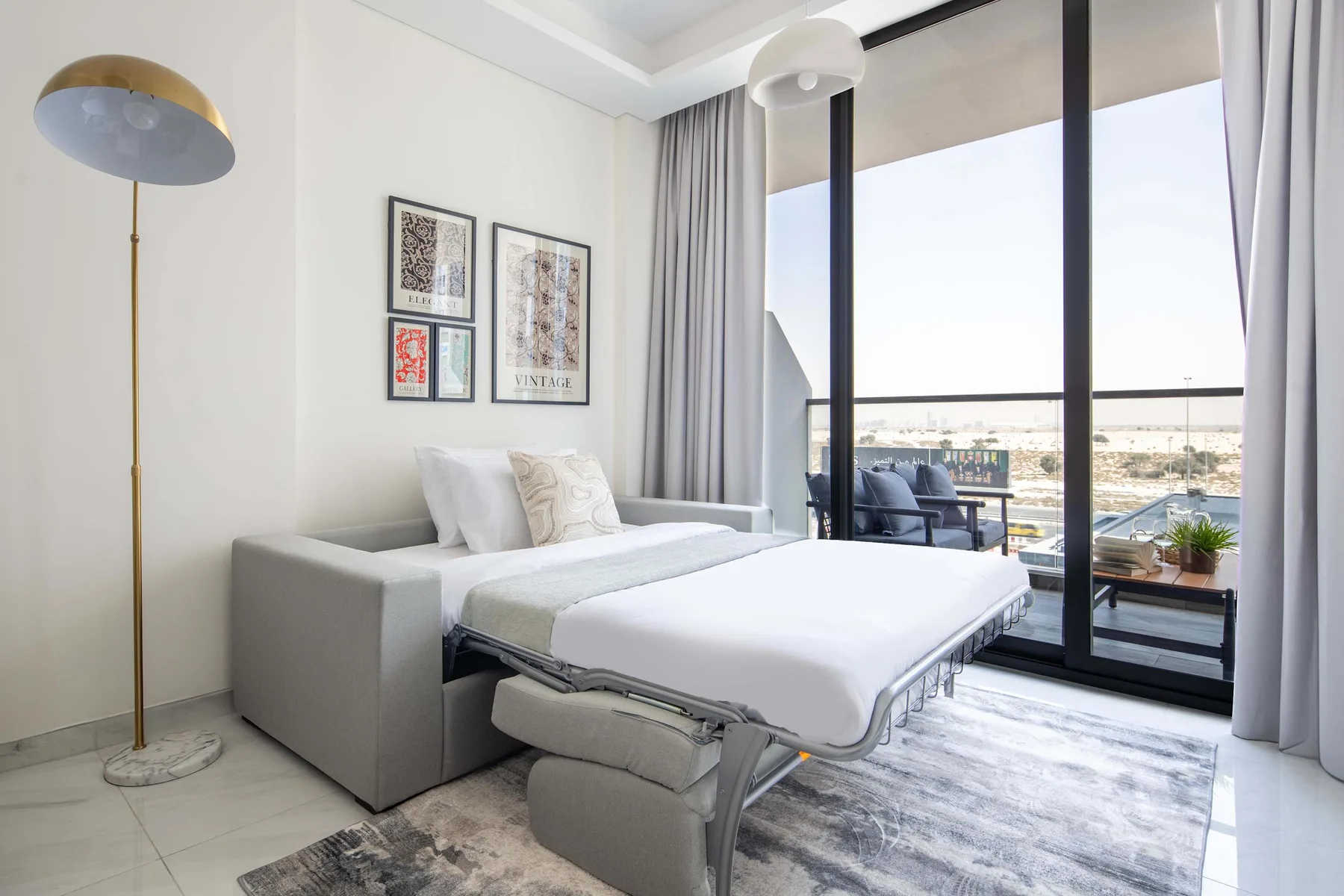 A bright bedroom with a bed, seating, and large windows overlooking the landscape.