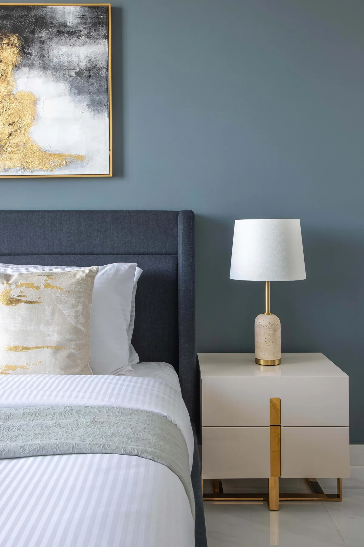 A bedroom with a bed, bedside table, and lamp against a blue-gray wall.