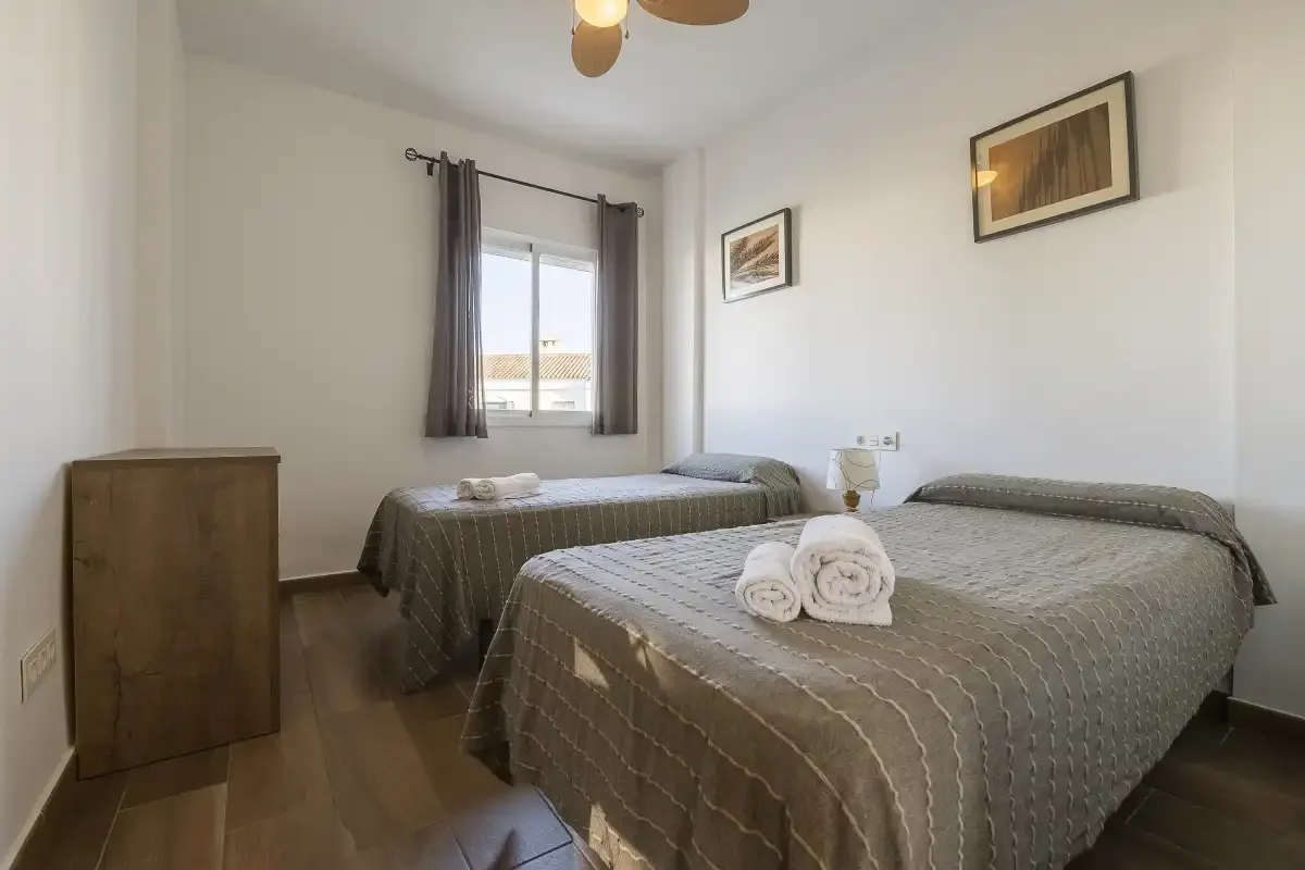 A bedroom with two beds, a window, and framed artwork.