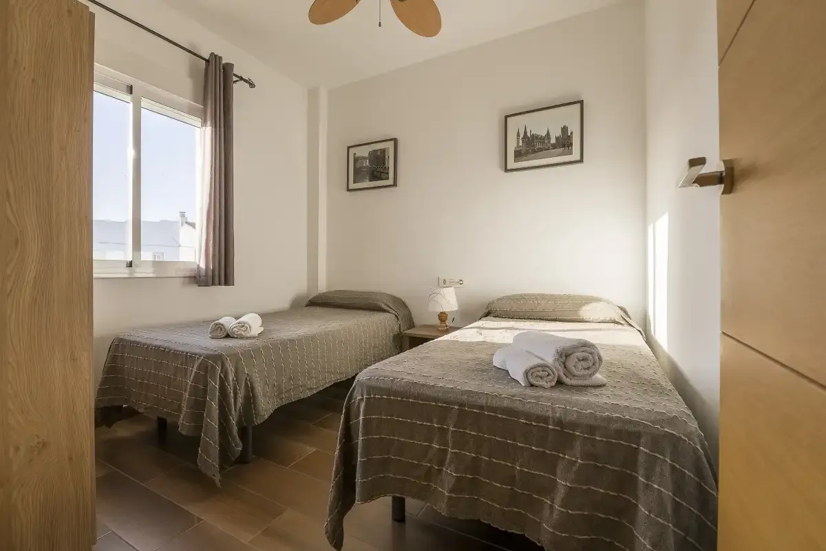 A bedroom with two beds, folded towels, and a window.