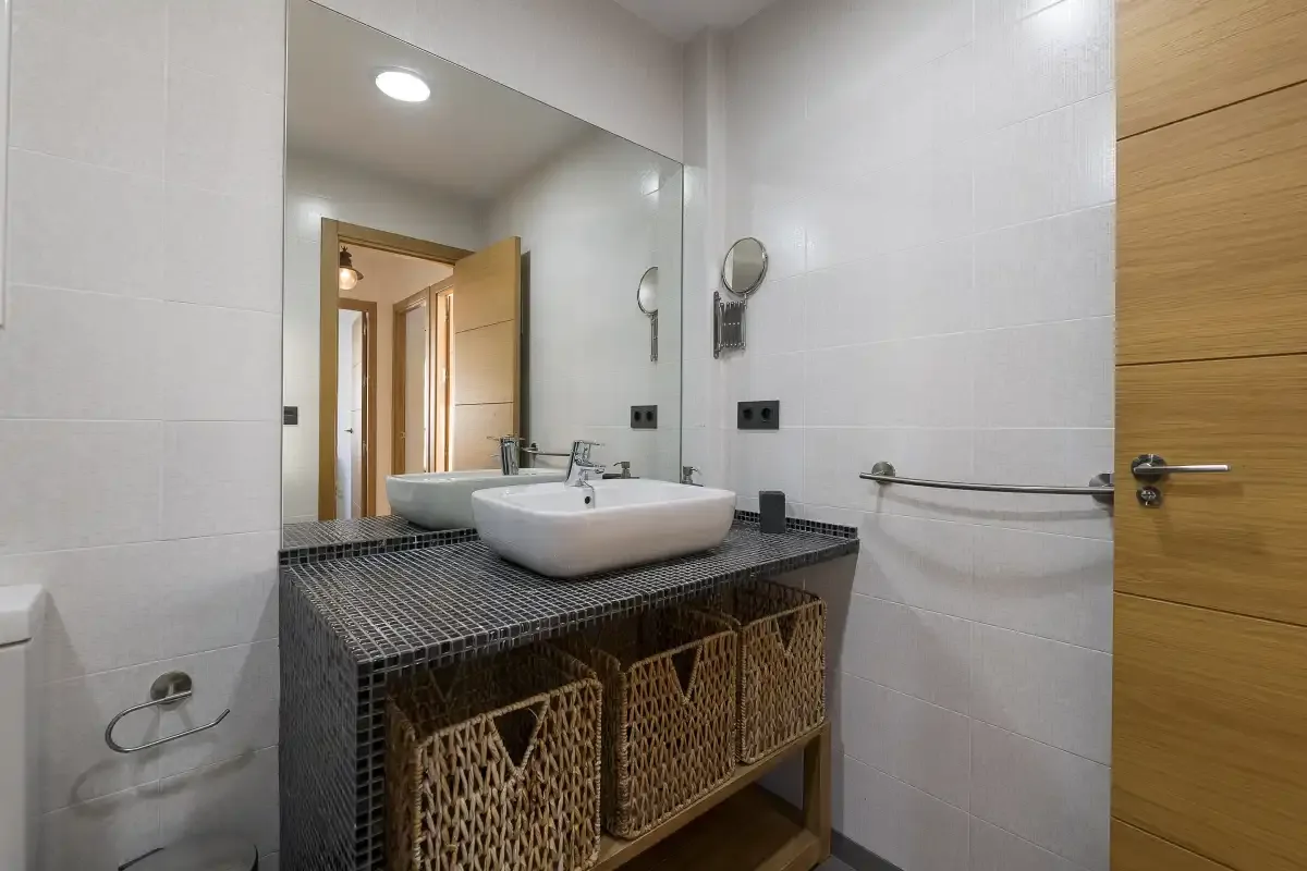 A tiled bathroom with a sink vanity, mirror, and open wooden door.