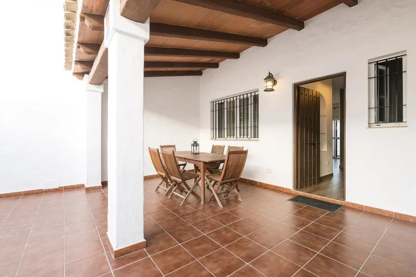 A covered patio with a wooden dining table and chairs beside a doorway.