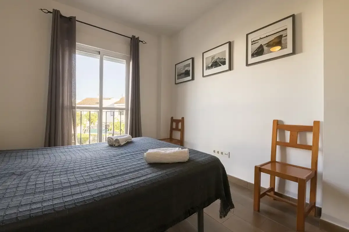 A bedroom with a bed, wooden chairs, and framed pictures on the wall.