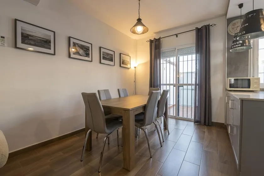 A dining area with a wooden table and chairs beside a curtained glass door.