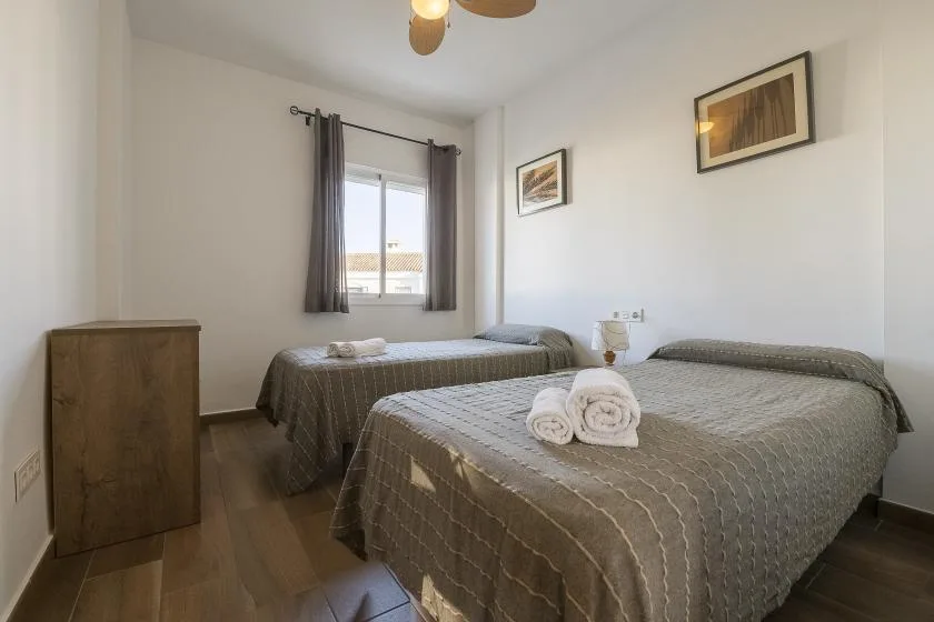 A bright bedroom with two beds, a window, and framed pictures on the walls.