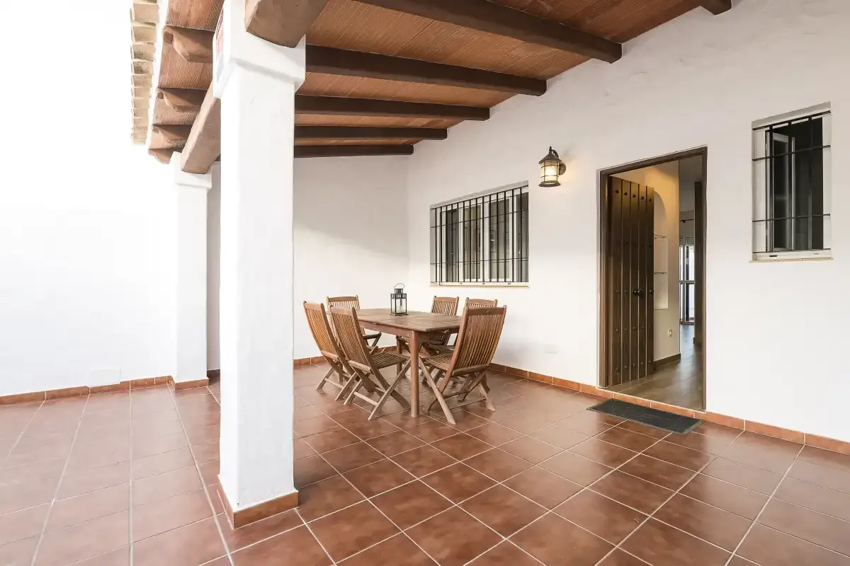 A covered patio with a wooden dining table and chairs beneath exposed beams.