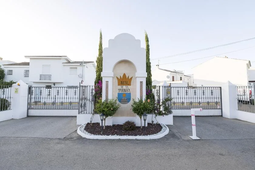 A white entrance arch with a decorative sign stands between gated sections of a property.