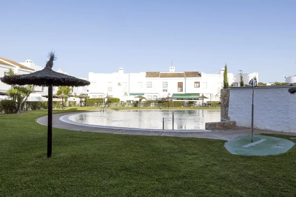A landscaped outdoor pool area with a grassy lawn and thatched shade umbrella.