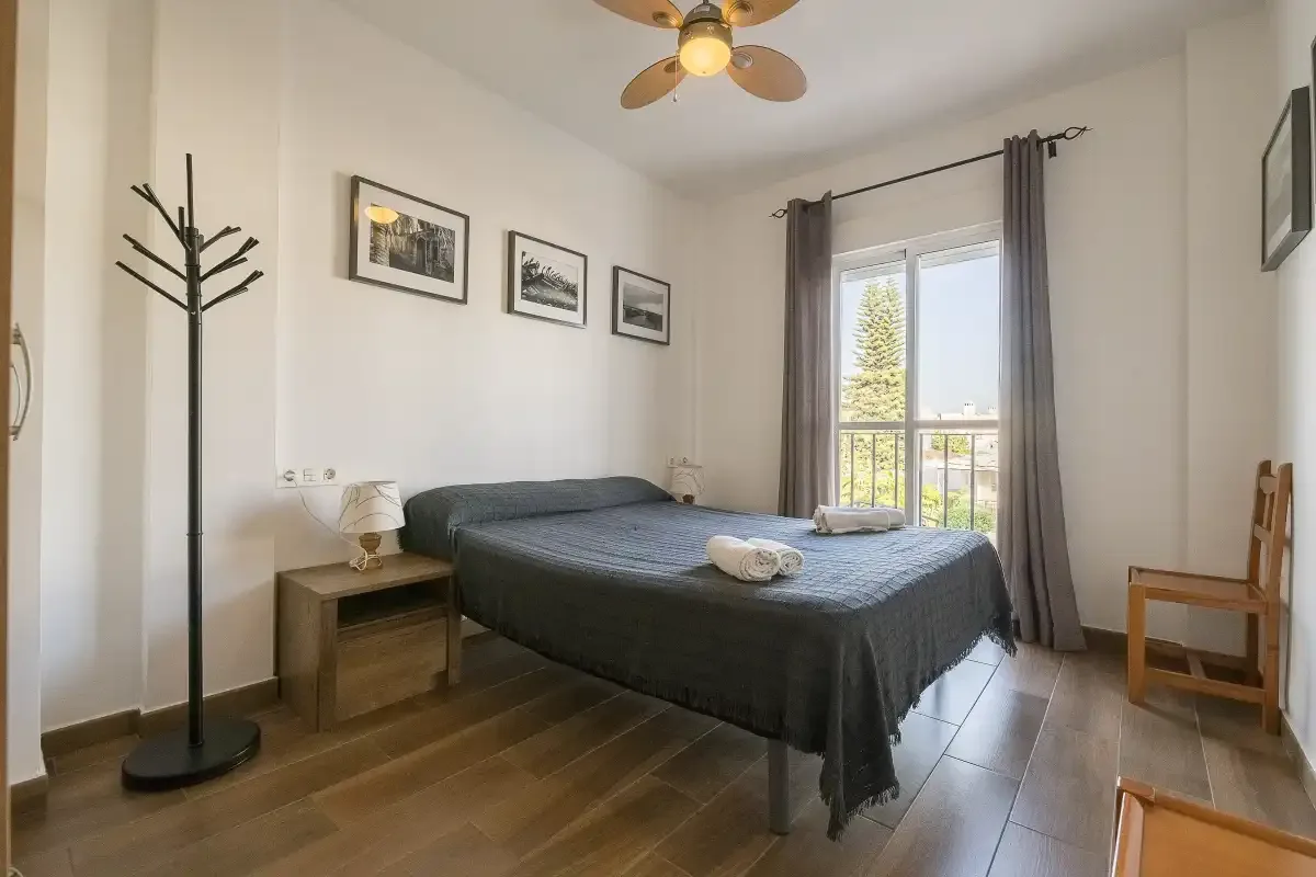 A bedroom with a double bed, bedside table, and balcony doors.