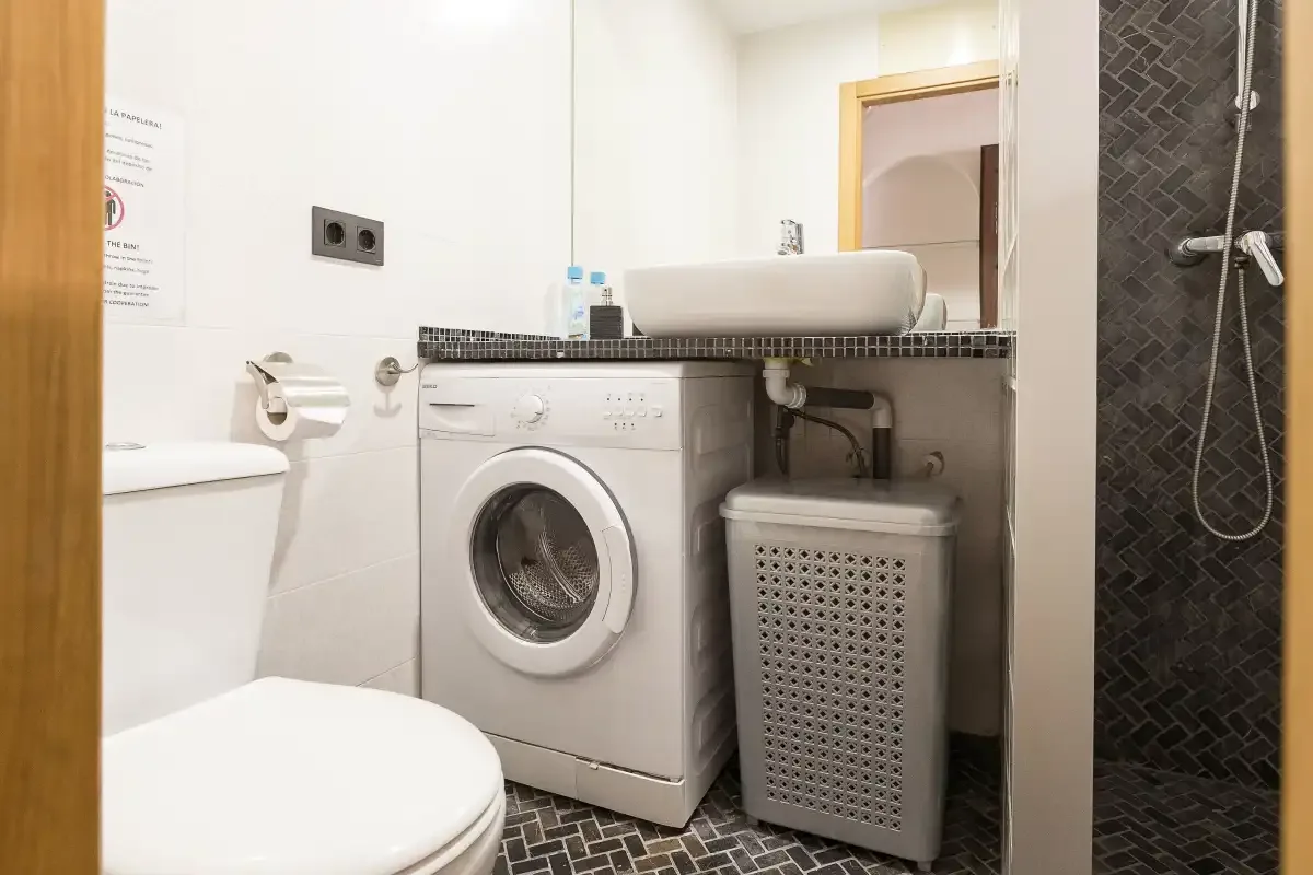 A bathroom with a washing machine, sink, toilet, and shower.