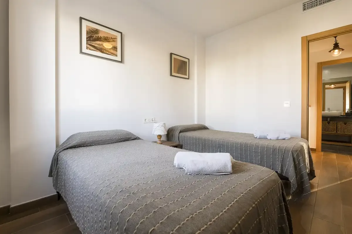 A bedroom with two beds, gray bedspreads, and framed pictures on the wall.